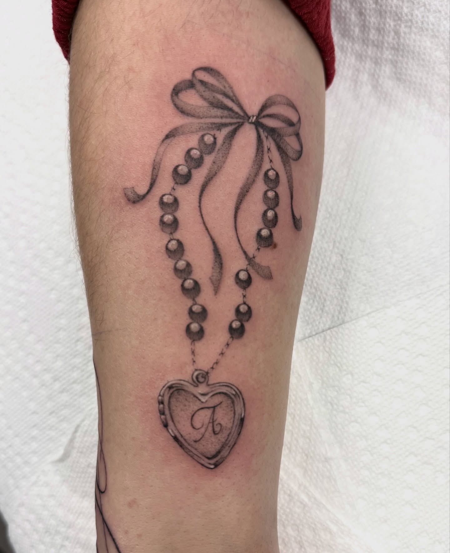 Beaded necklace with heart locket black and grey tattoo on the forearm by dinah