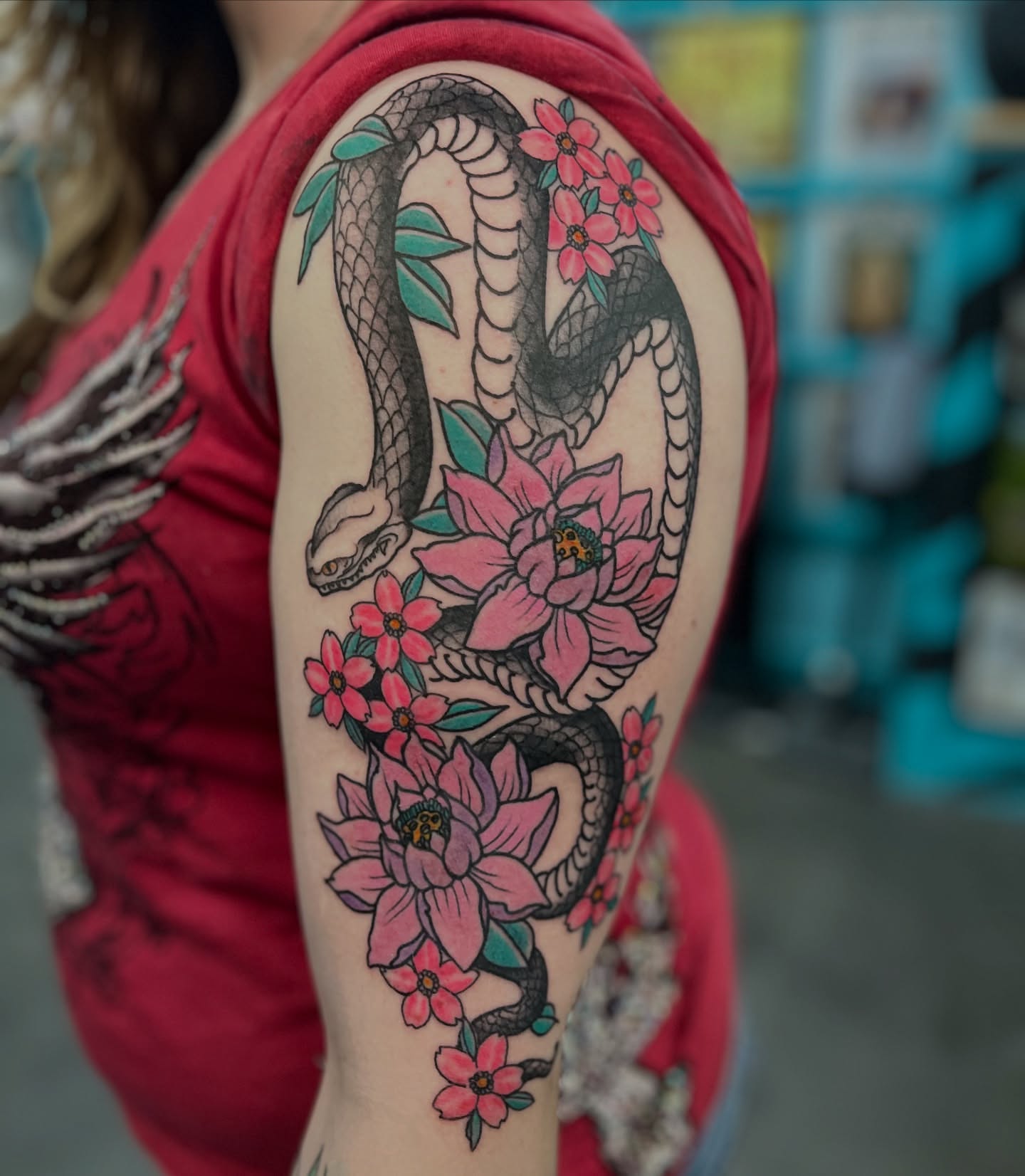 Snake and flowers American traditional tattoo on the upper arm by Ashley Camp