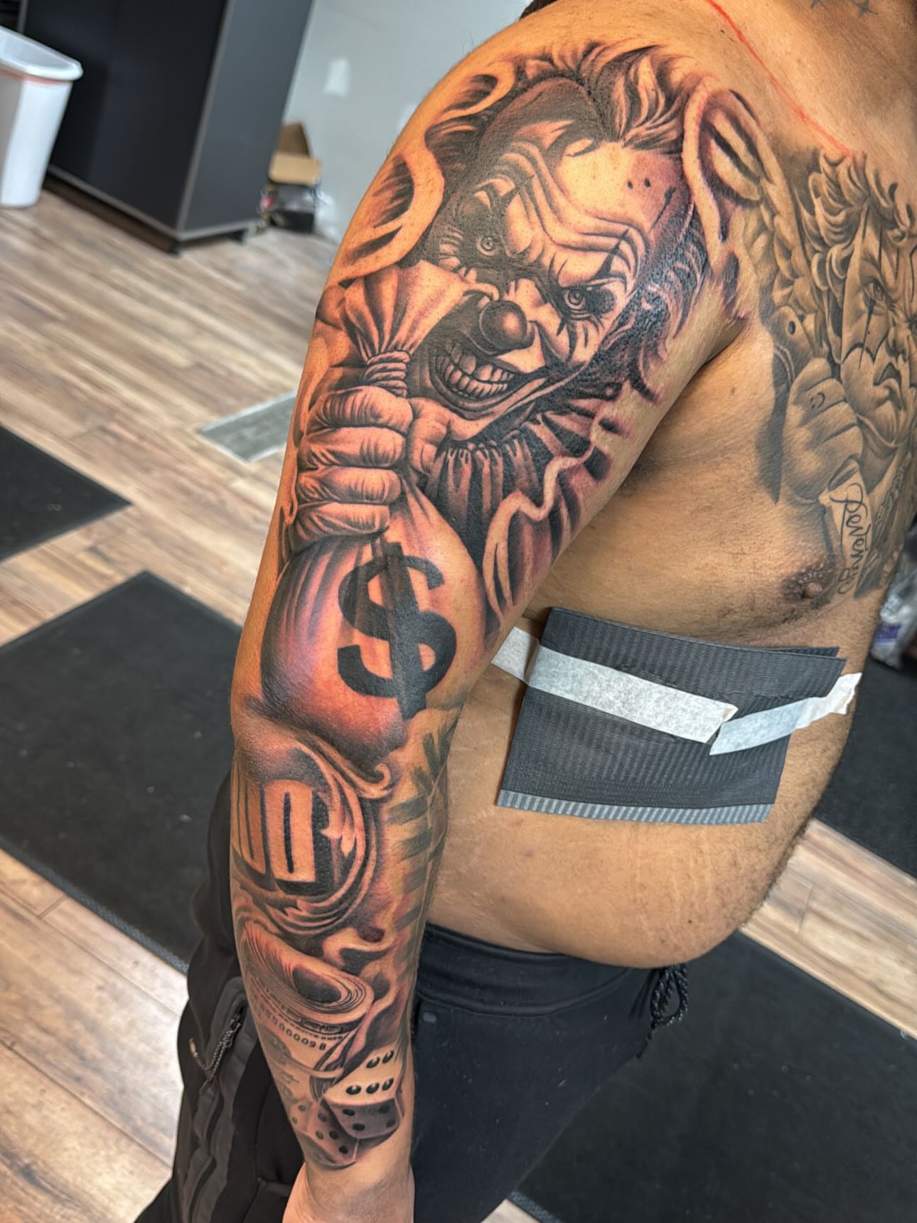 Clown holding money realism tattoo on the upper arm by Cedric Fleming