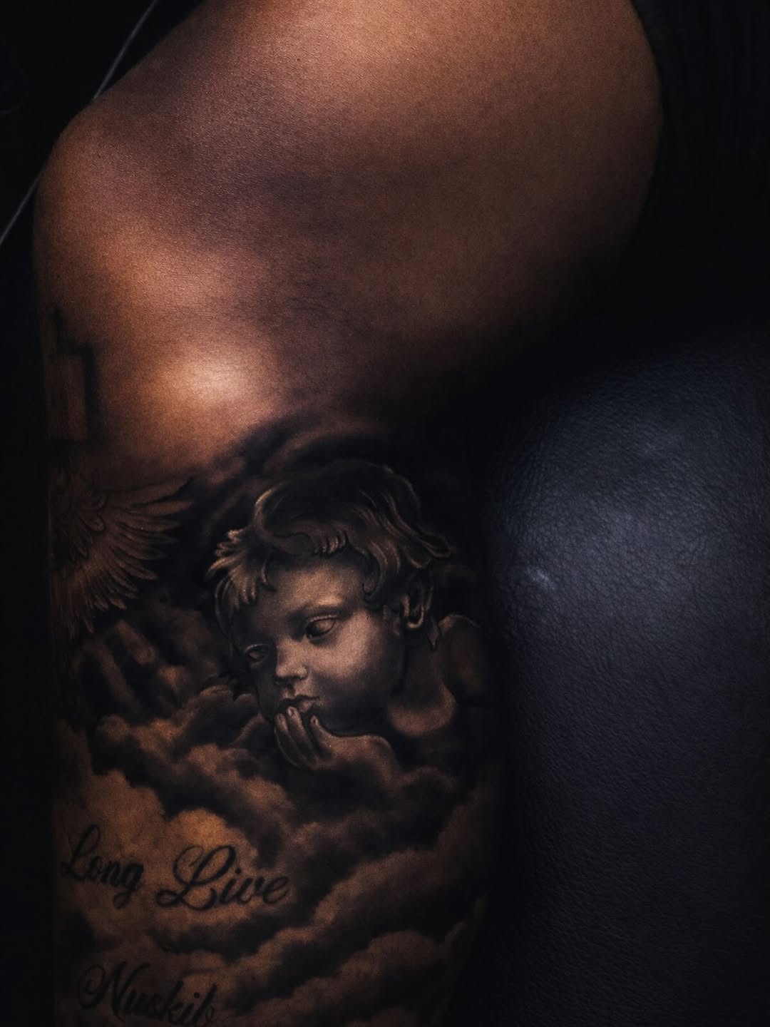 Cherub with clouds and lettering realism tattoo on the upper arm by Rico Rosario