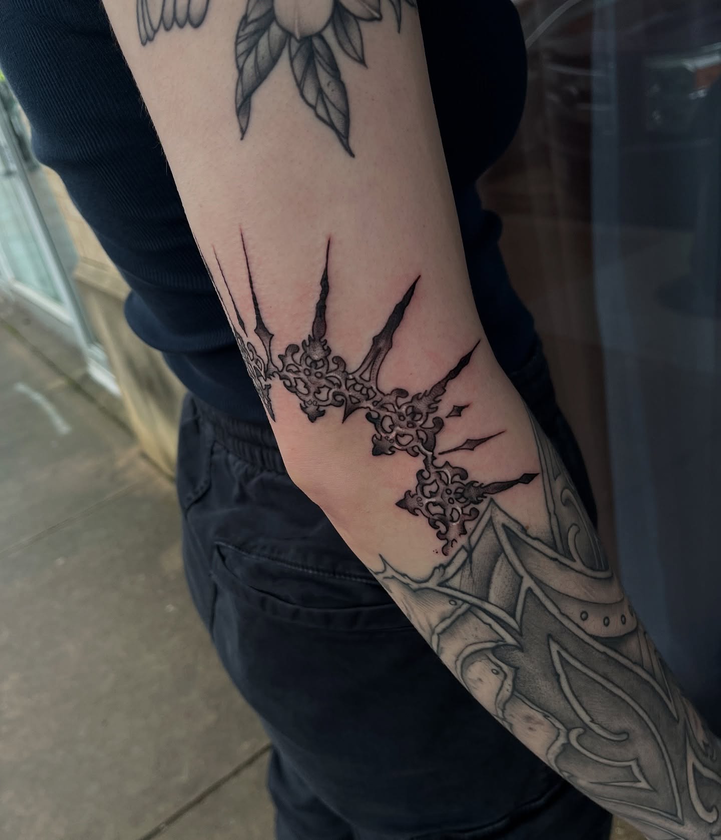 Cross with spikes black and grey tattoo on the forearm by Timmy