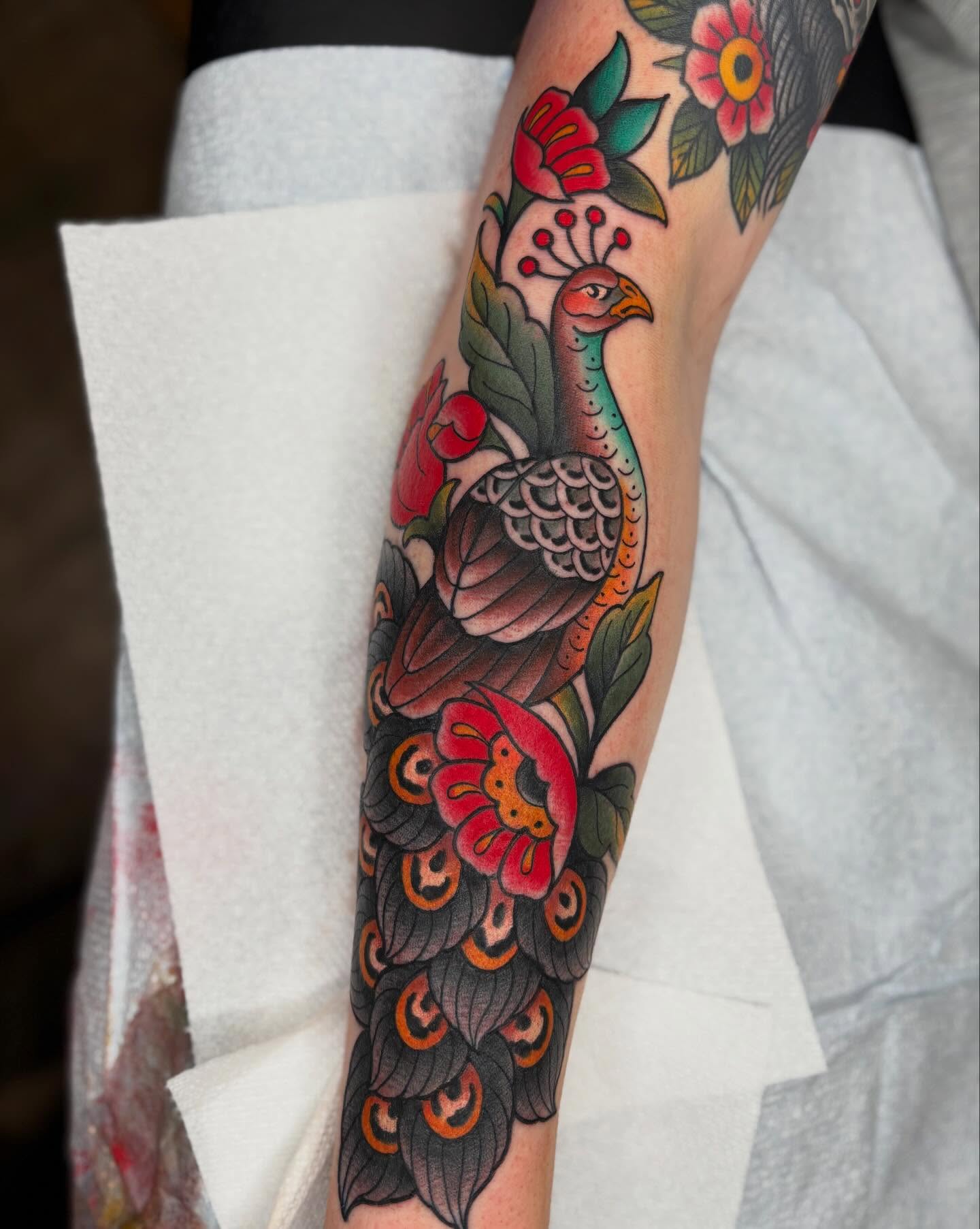 Peacock and flowers American traditional tattoo on the forearm by Cody Collins