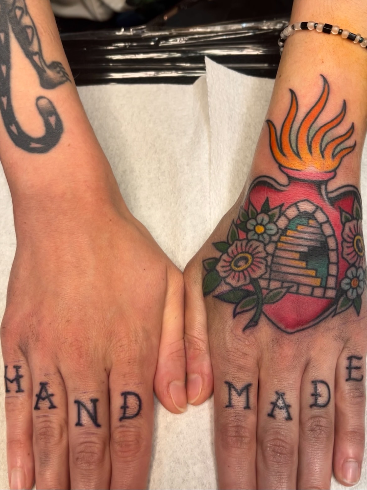 Heart with flame American traditional tattoo on the hand by Macy Bird