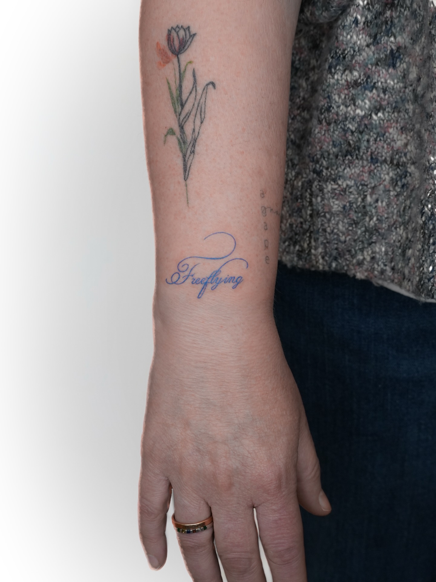 Flower and script fine line tattoo on the forearm by Jena