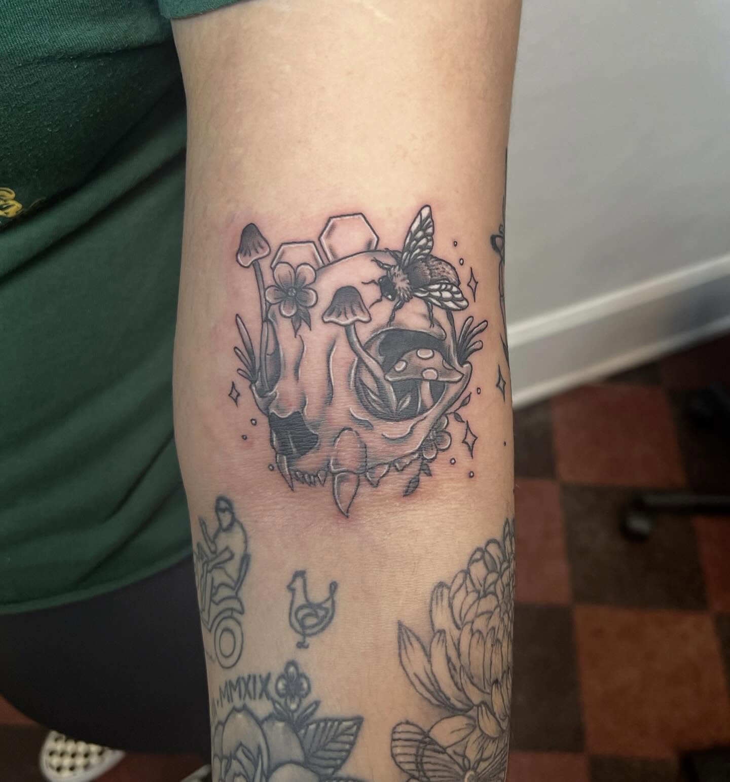 Skull with mushrooms and flowers black and grey tattoo on the forearm by Amber Rose