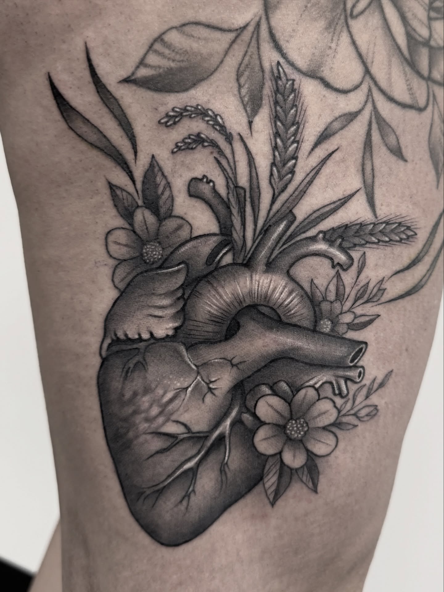Anatomical heart with floral elements black and grey tattoo on the thigh by Jaxx Kesler