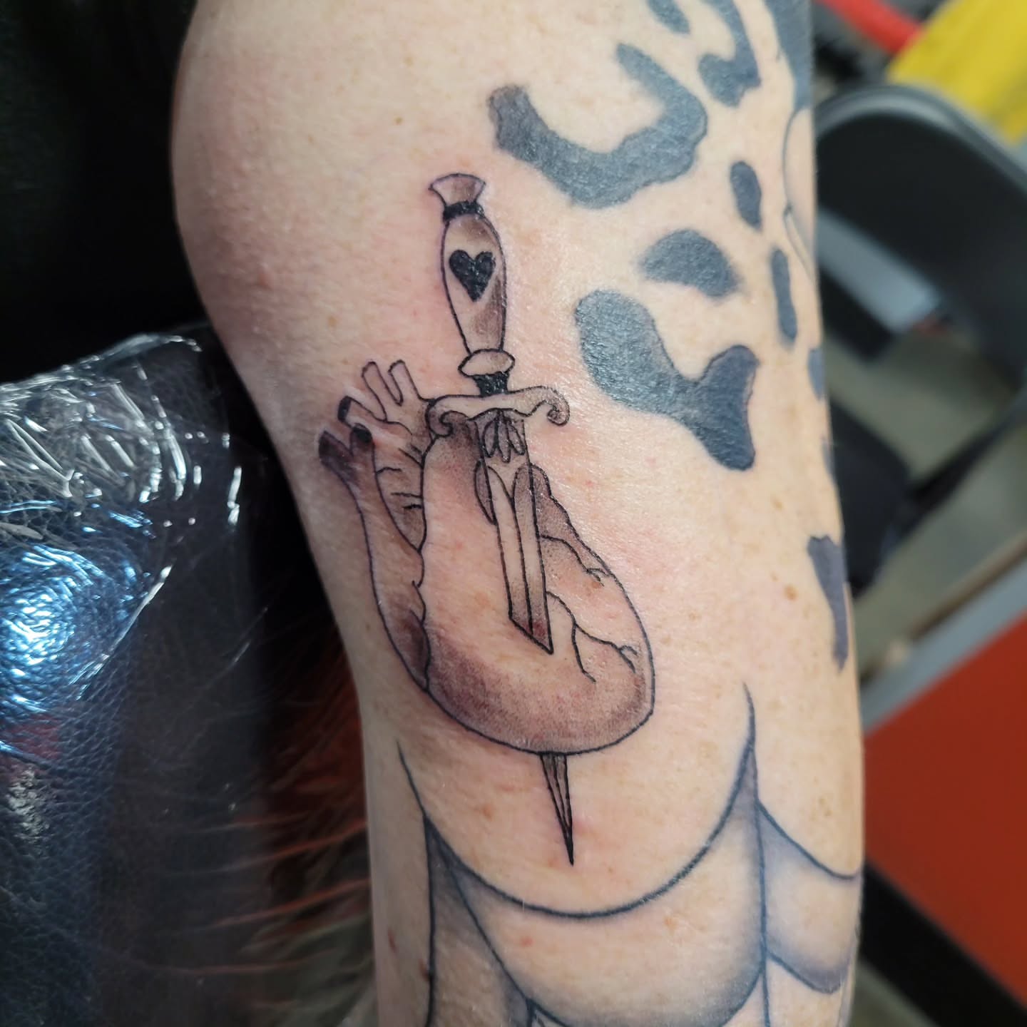 Heart with dagger black and grey tattoo on the forearm by Aspen C