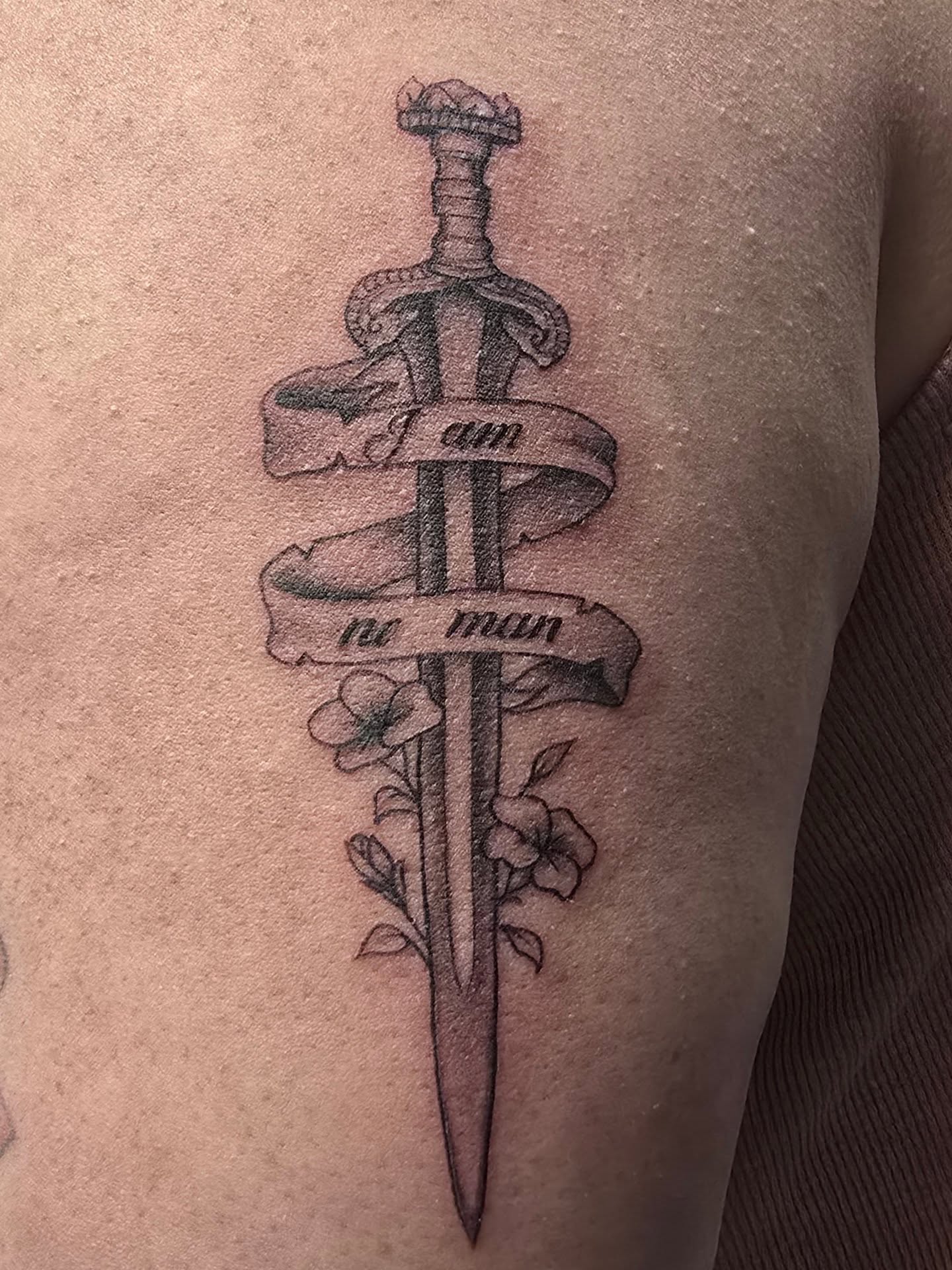 Sword and banner black and grey tattoo on the upper arm by Trinity