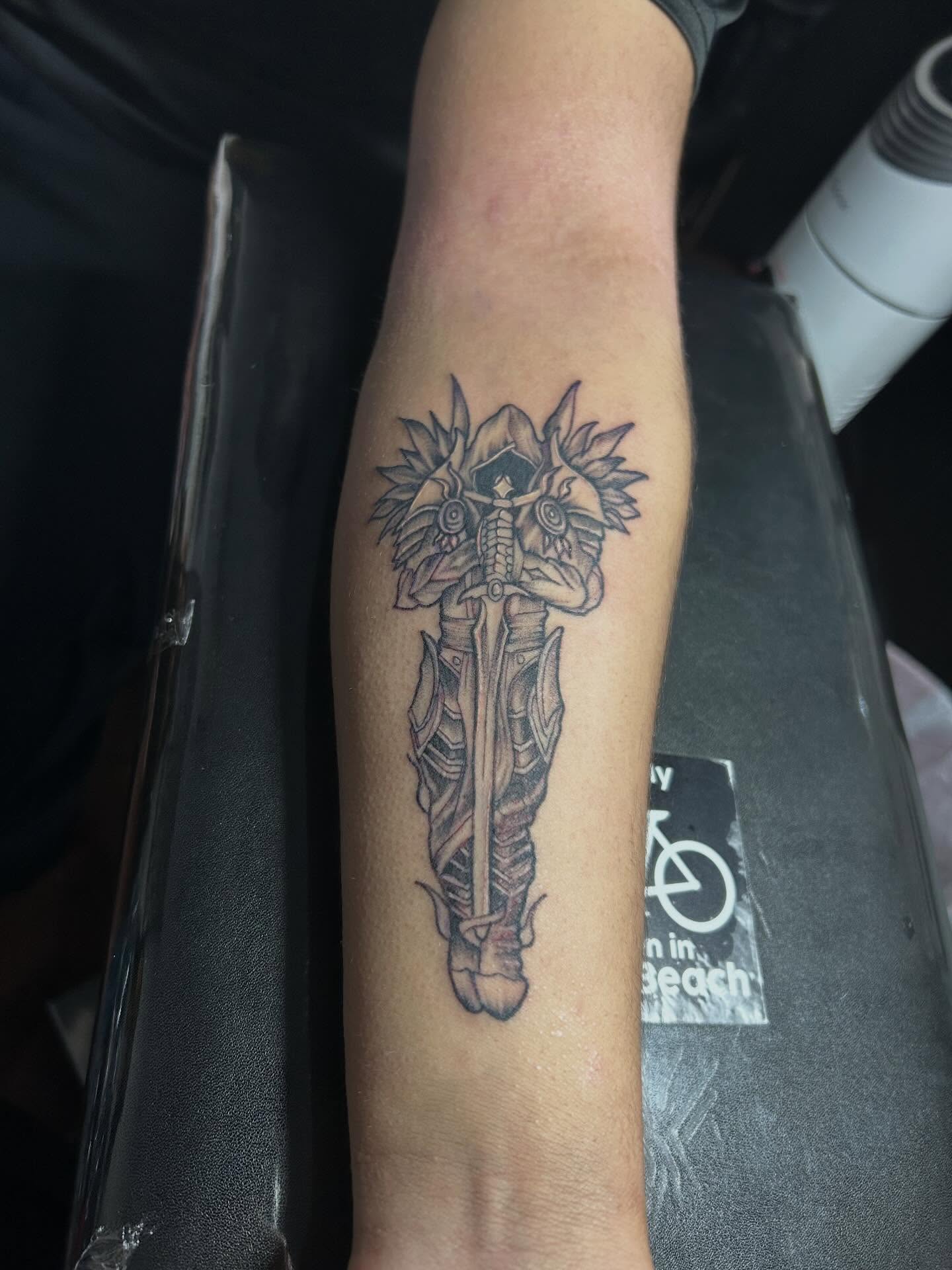 Mask with sword black and grey tattoo on the forearm by Felix perez (Tattooer)