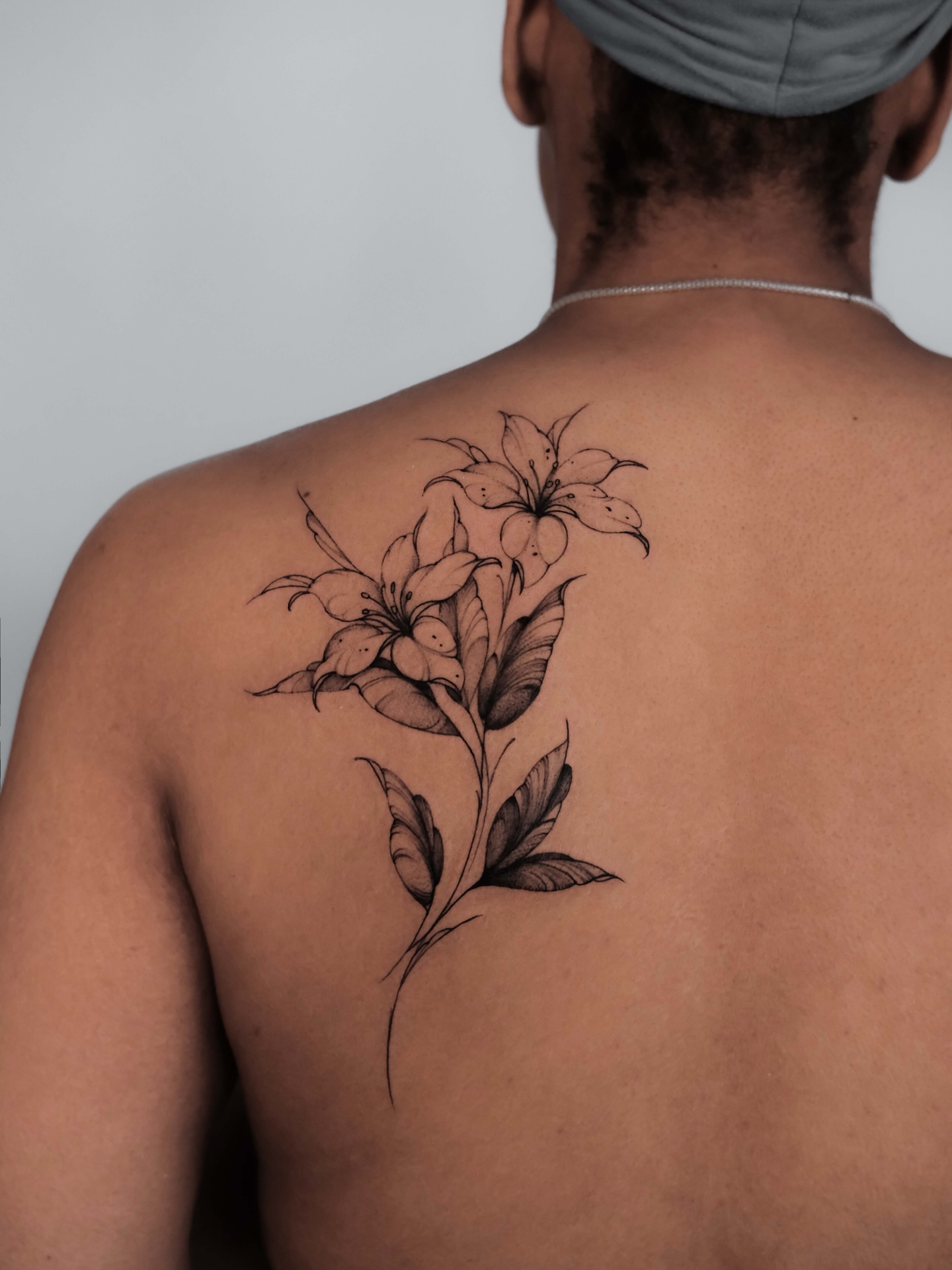 Lilies black and grey tattoo on the back by Anastasiia