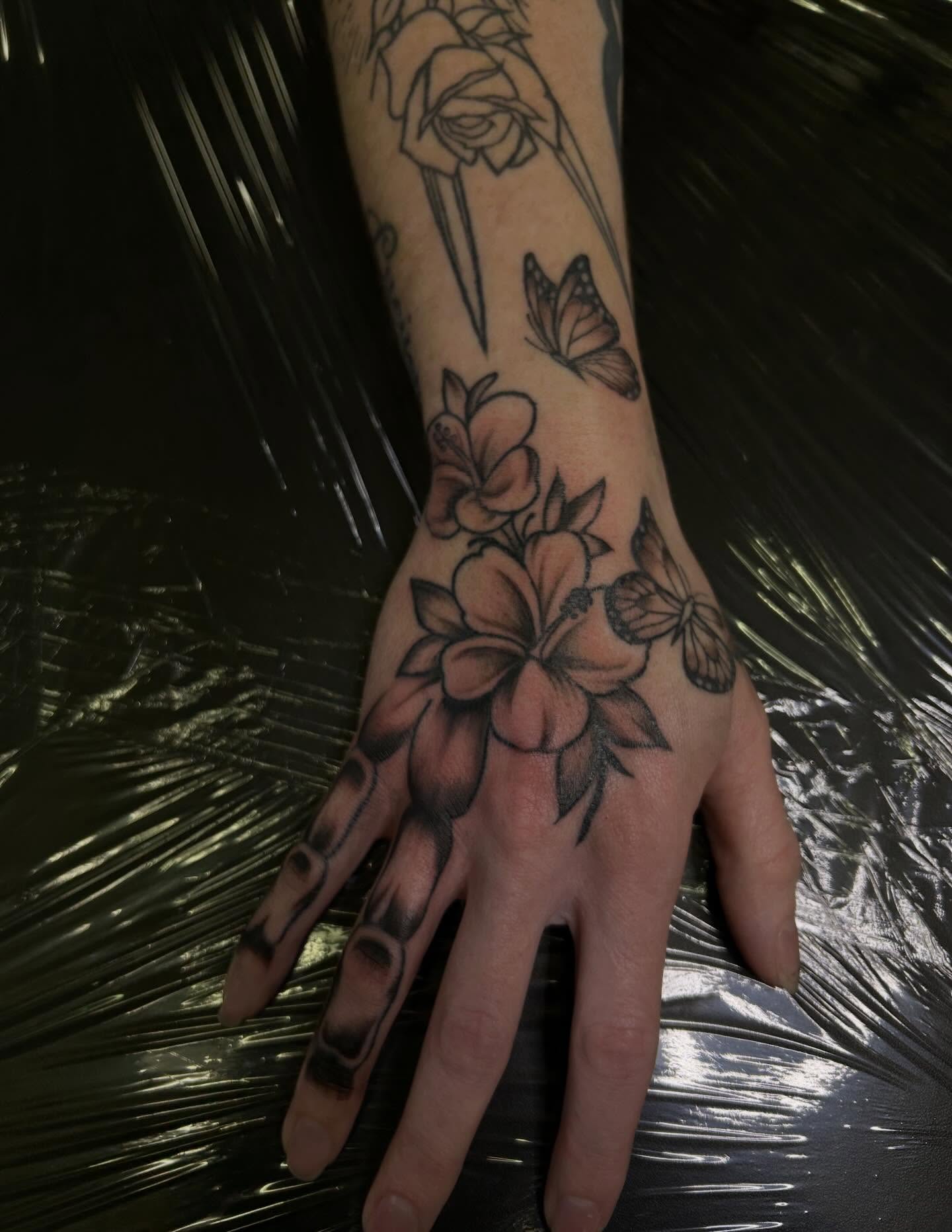 Flowers and butterflies black and grey tattoo on the hand by Victoria Mendez