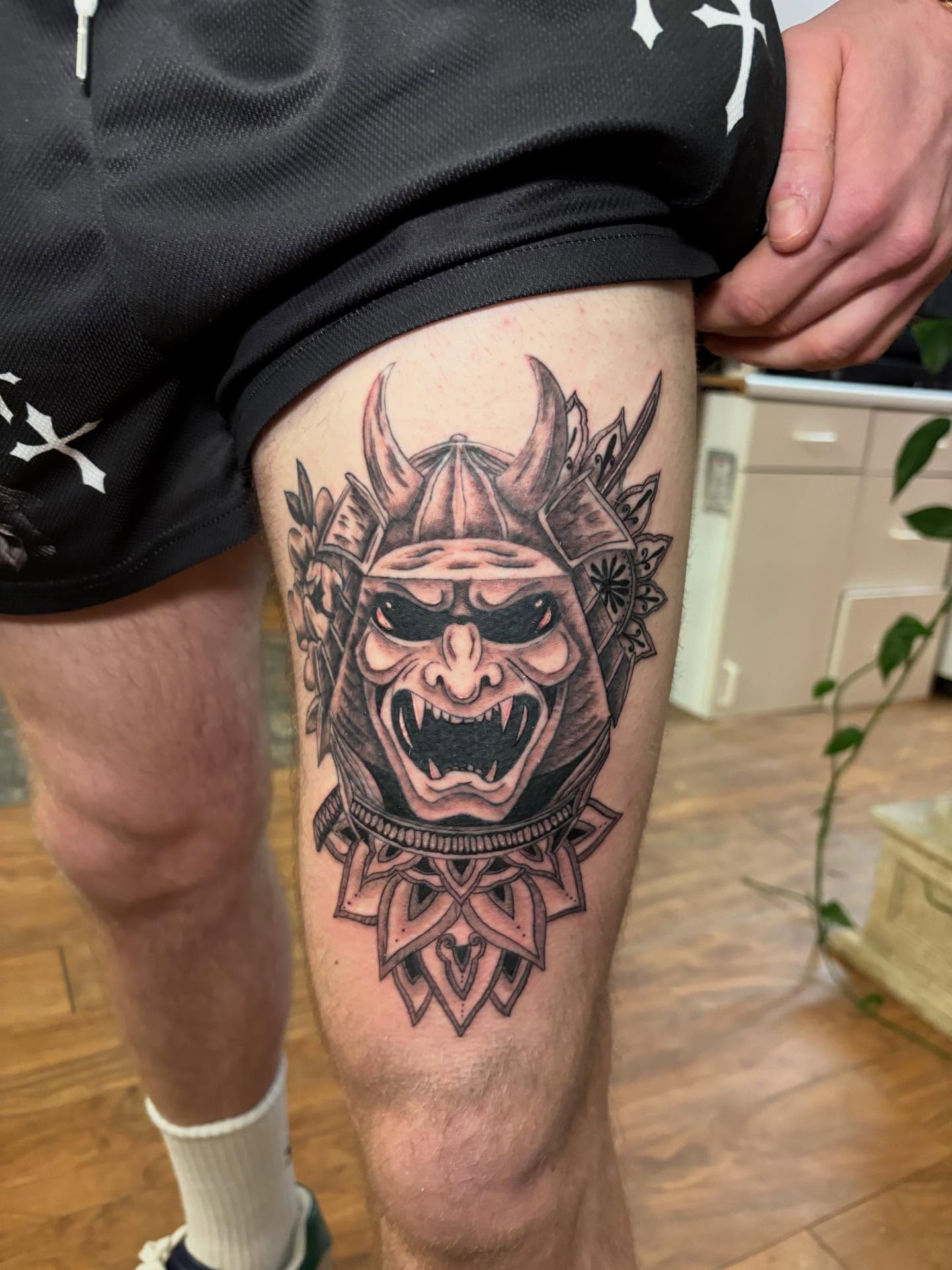 Demon mask black and grey tattoo on the thigh by Luke