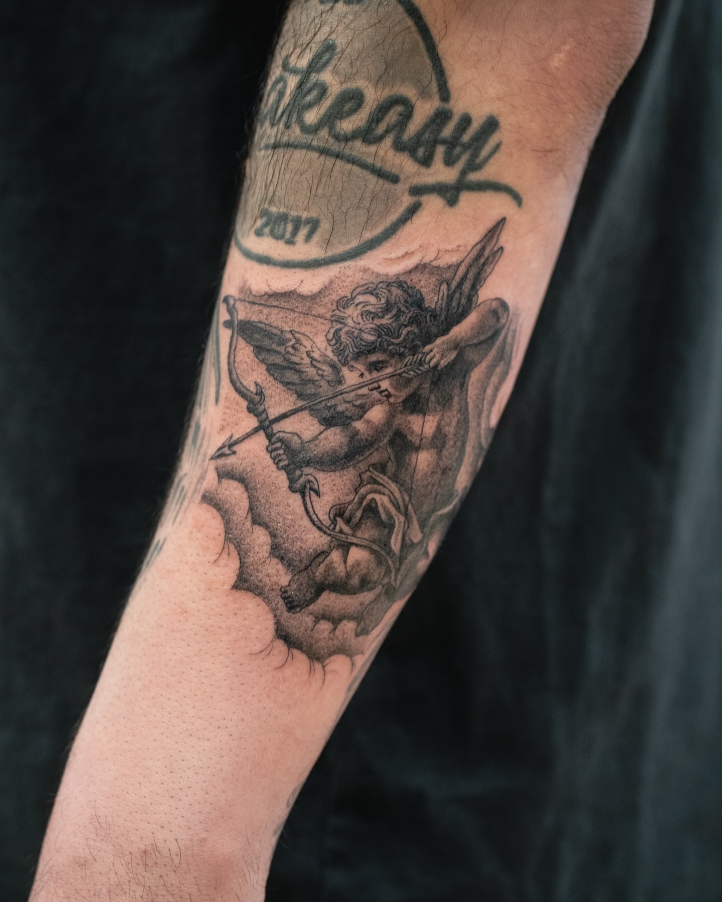 Cherub with bow and arrow black and grey tattoo on the forearm by James Fernella, San Francisco, California