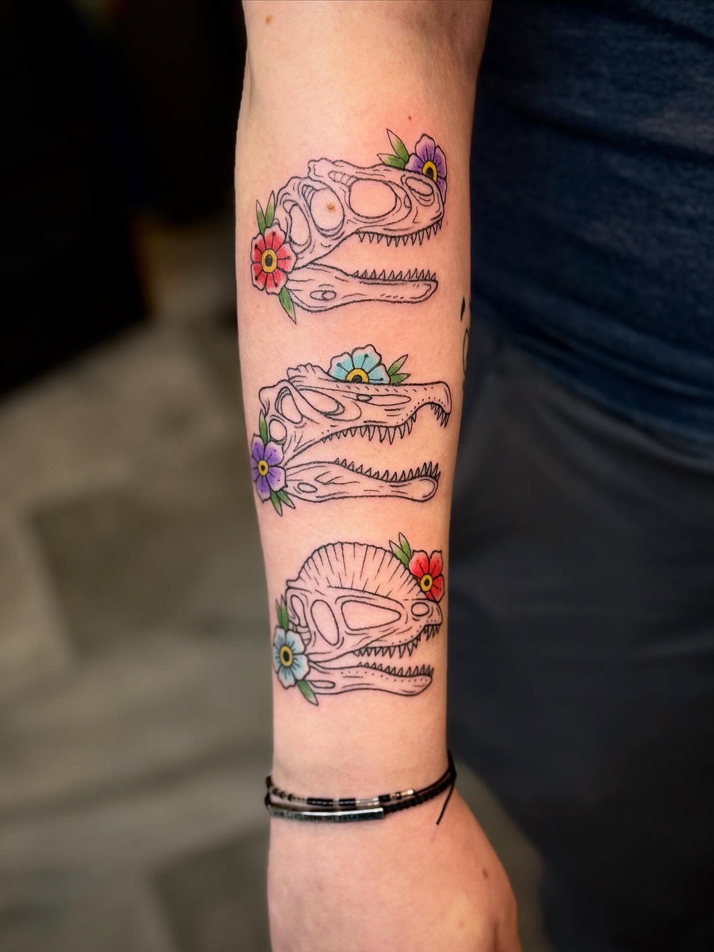 Dinosaur skulls with flowers American traditional tattoo on the forearm by Ashley Kayser
