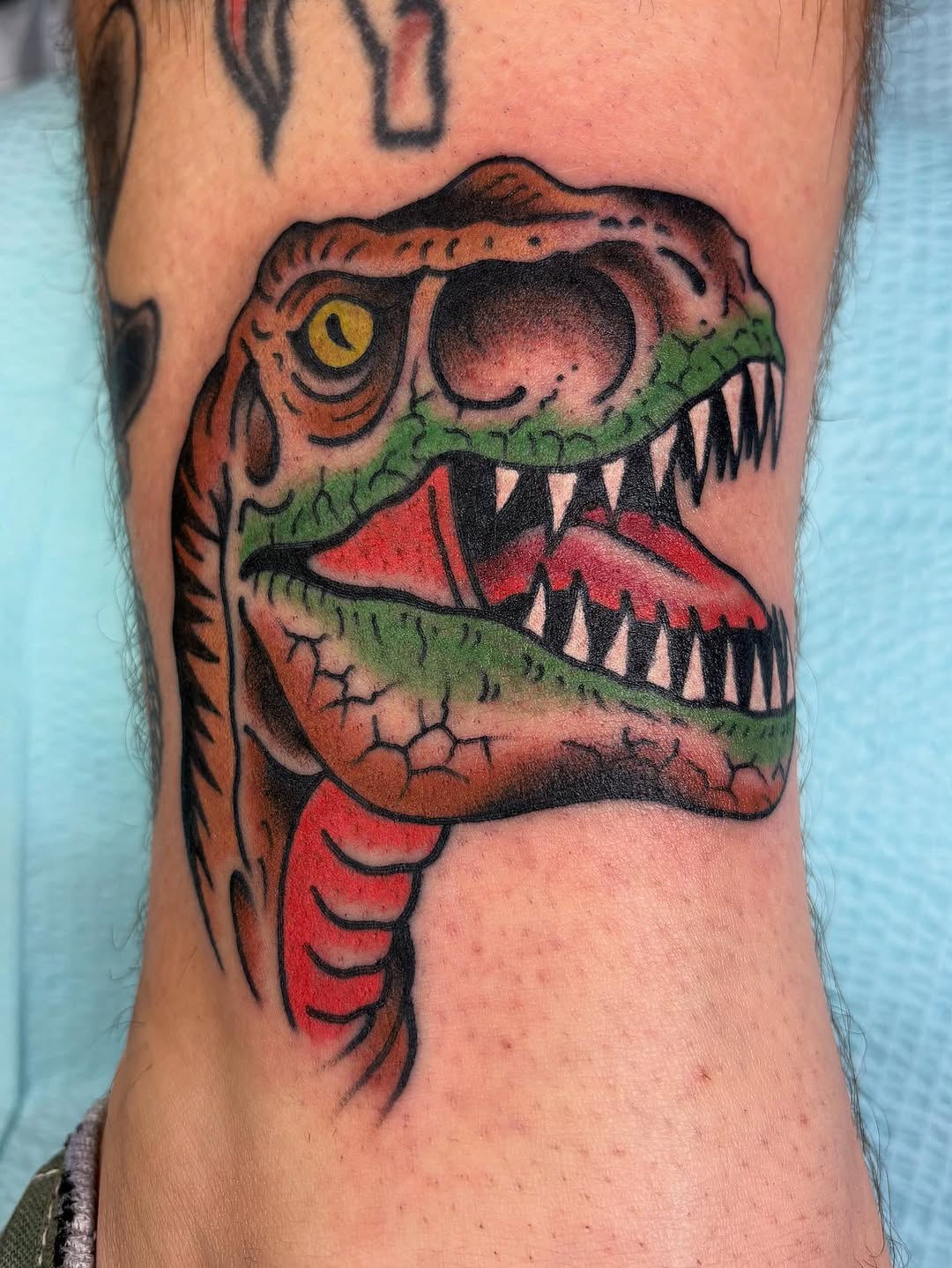 Dinosaur head American traditional tattoo on the forearm by Tom Wenzell