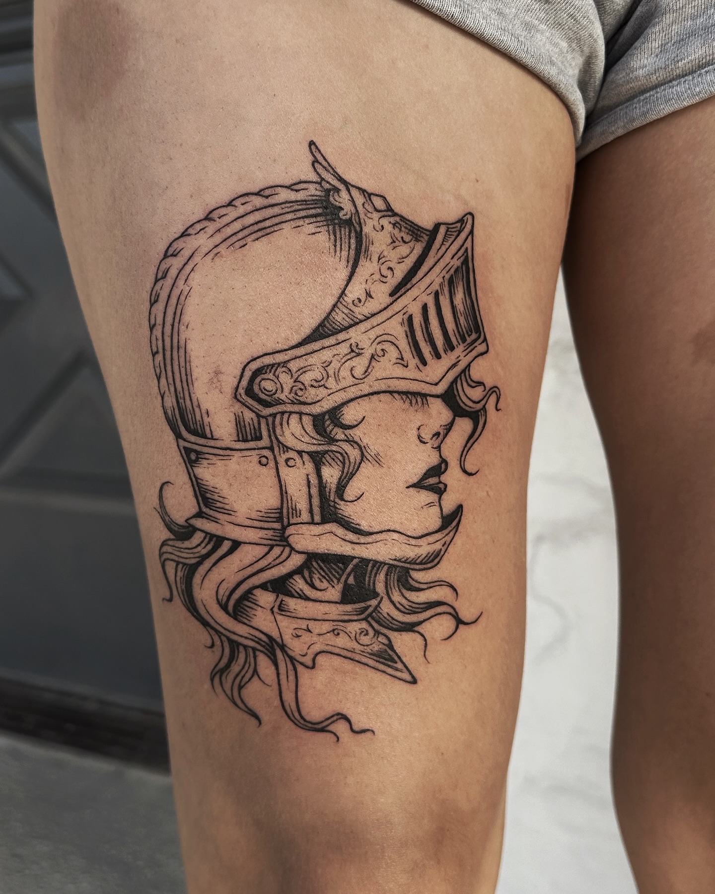 Woman with helmet black and grey tattoo on the thigh by Micky, Austin, Texas