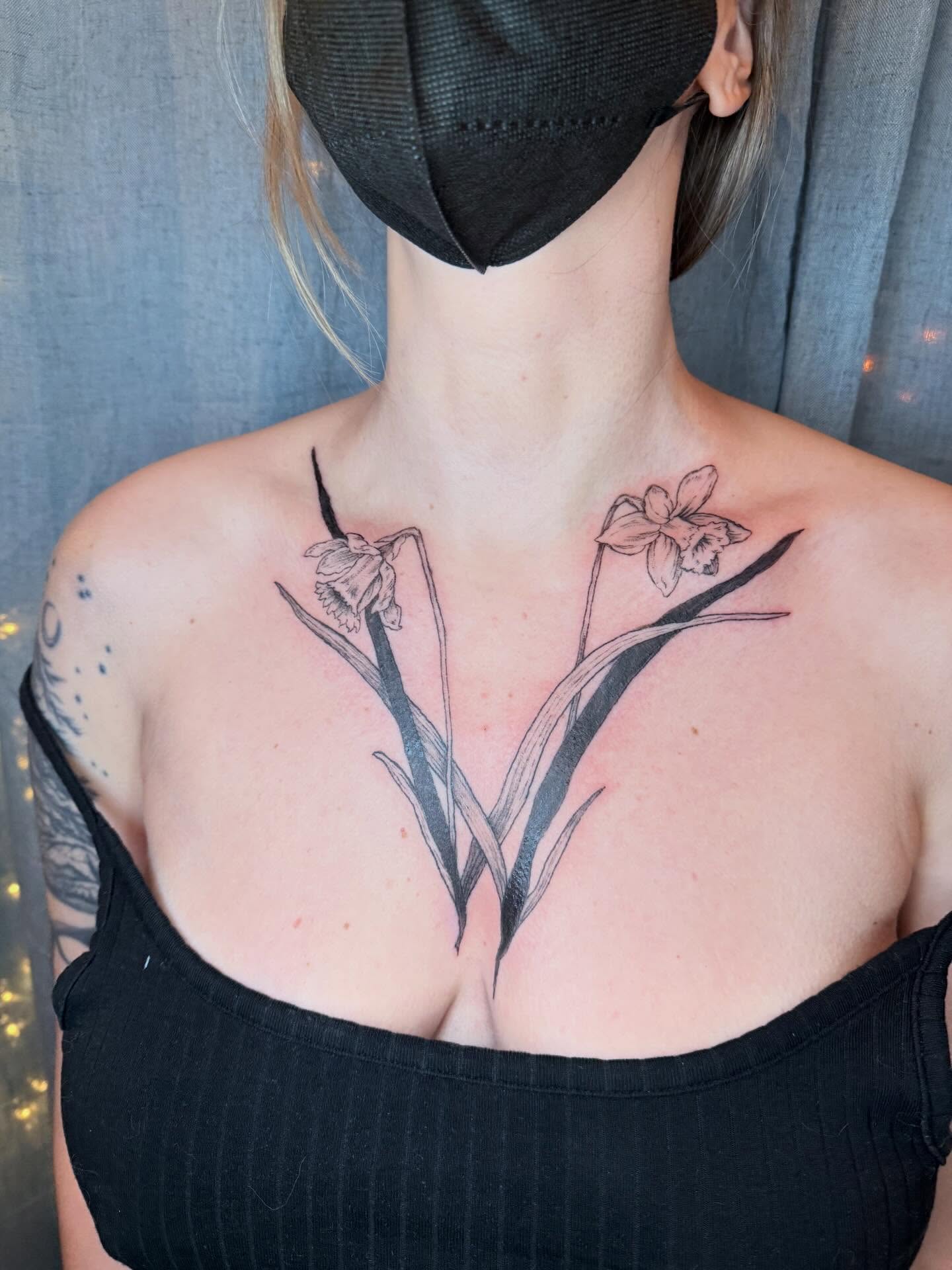 Daffodil and leaves black and grey tattoo on the chest by Emily Rose Lumsdaine