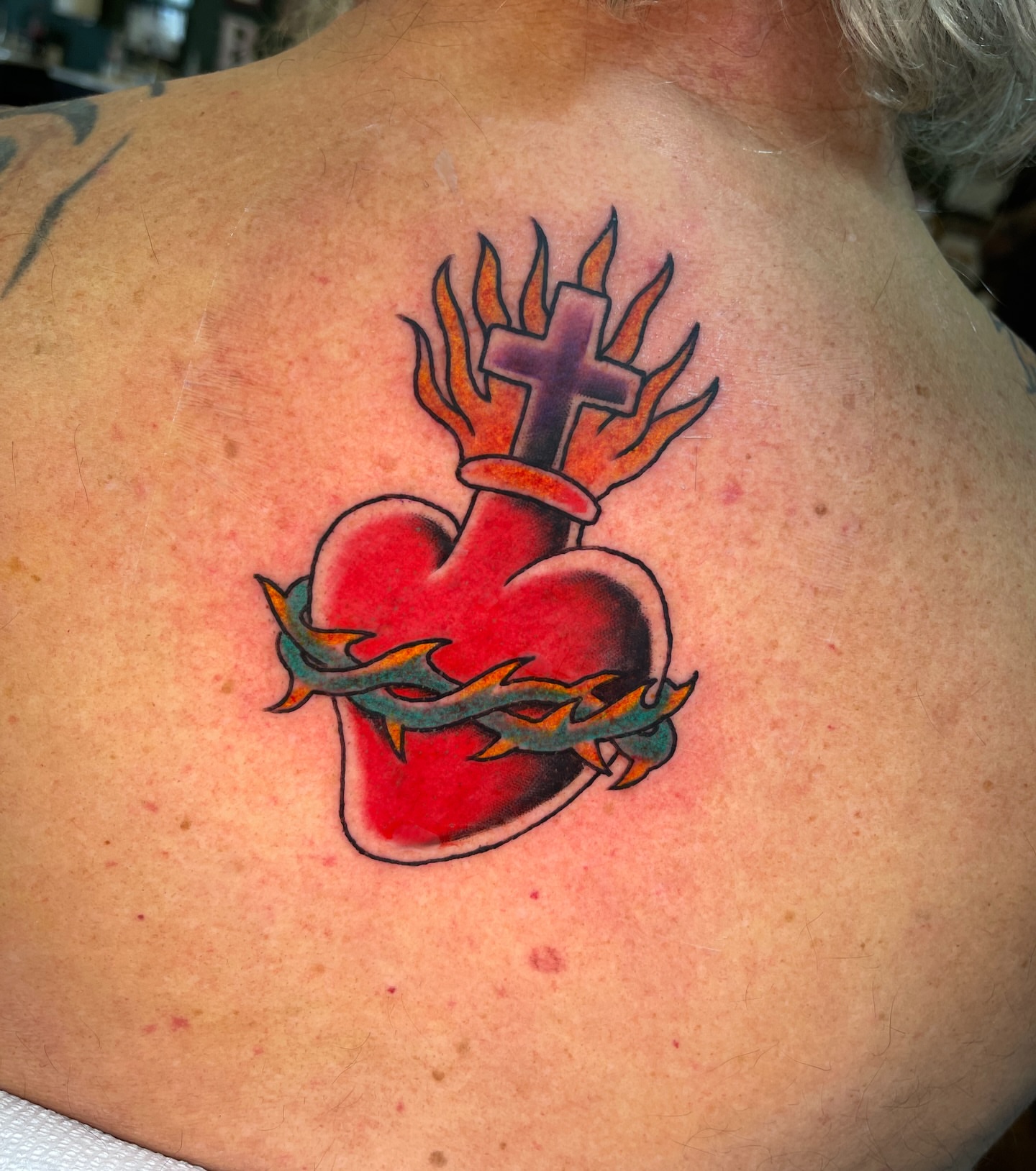 Heart with cross and flames American traditional tattoo on the back by Blake Alan Tattoos (TROUT)