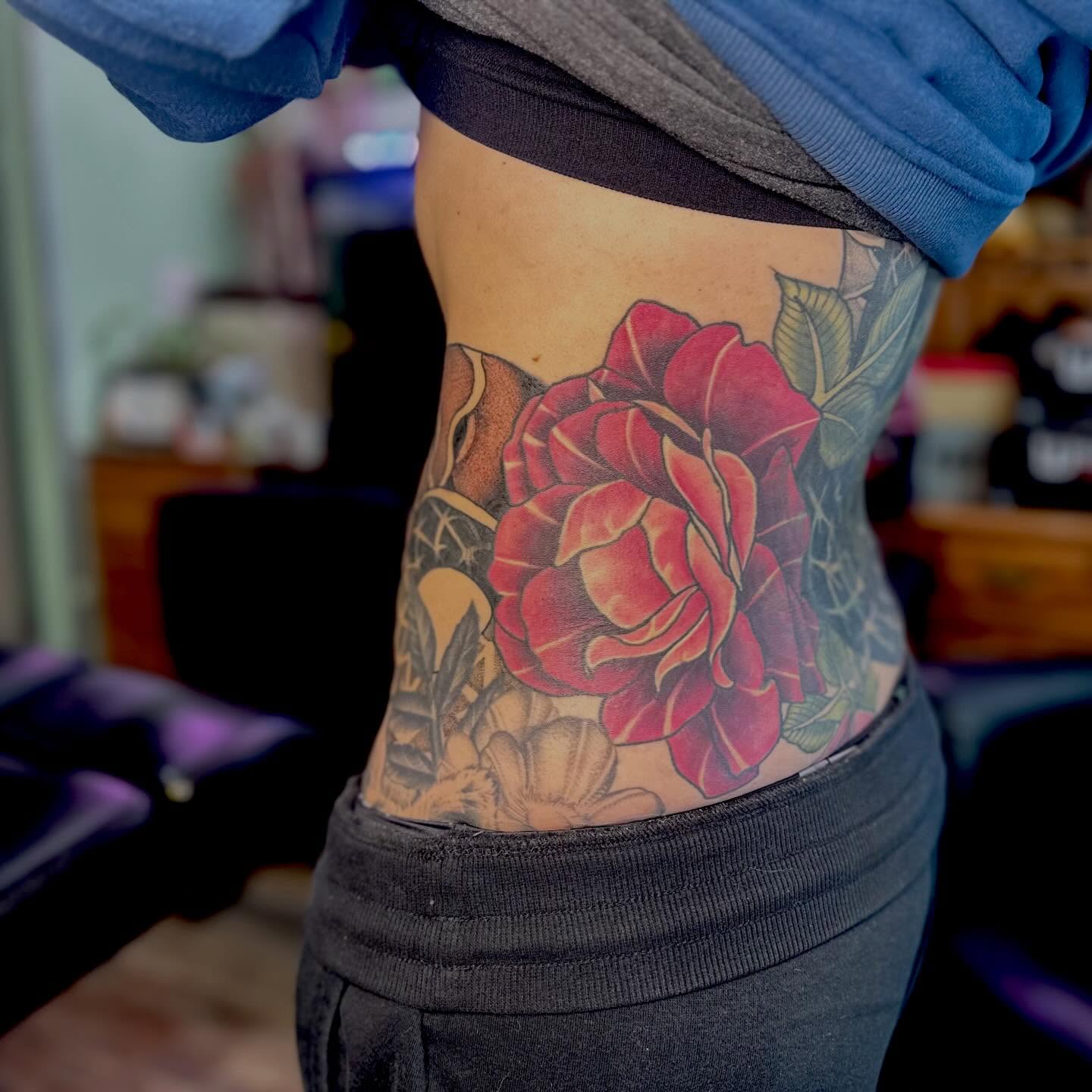Red rose realism tattoo on the torso by Leeuh Vandever