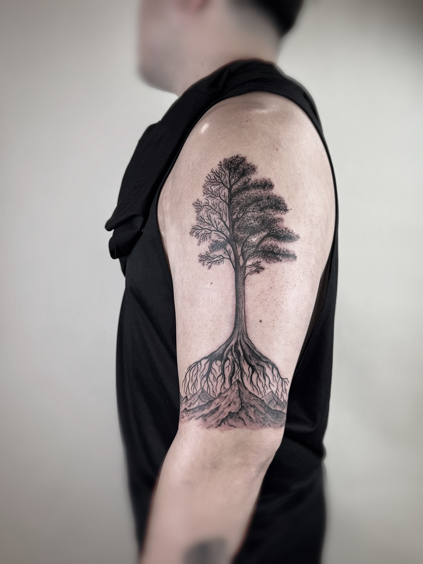 Tree black and grey tattoo on the upper arm by Jadyn Pang