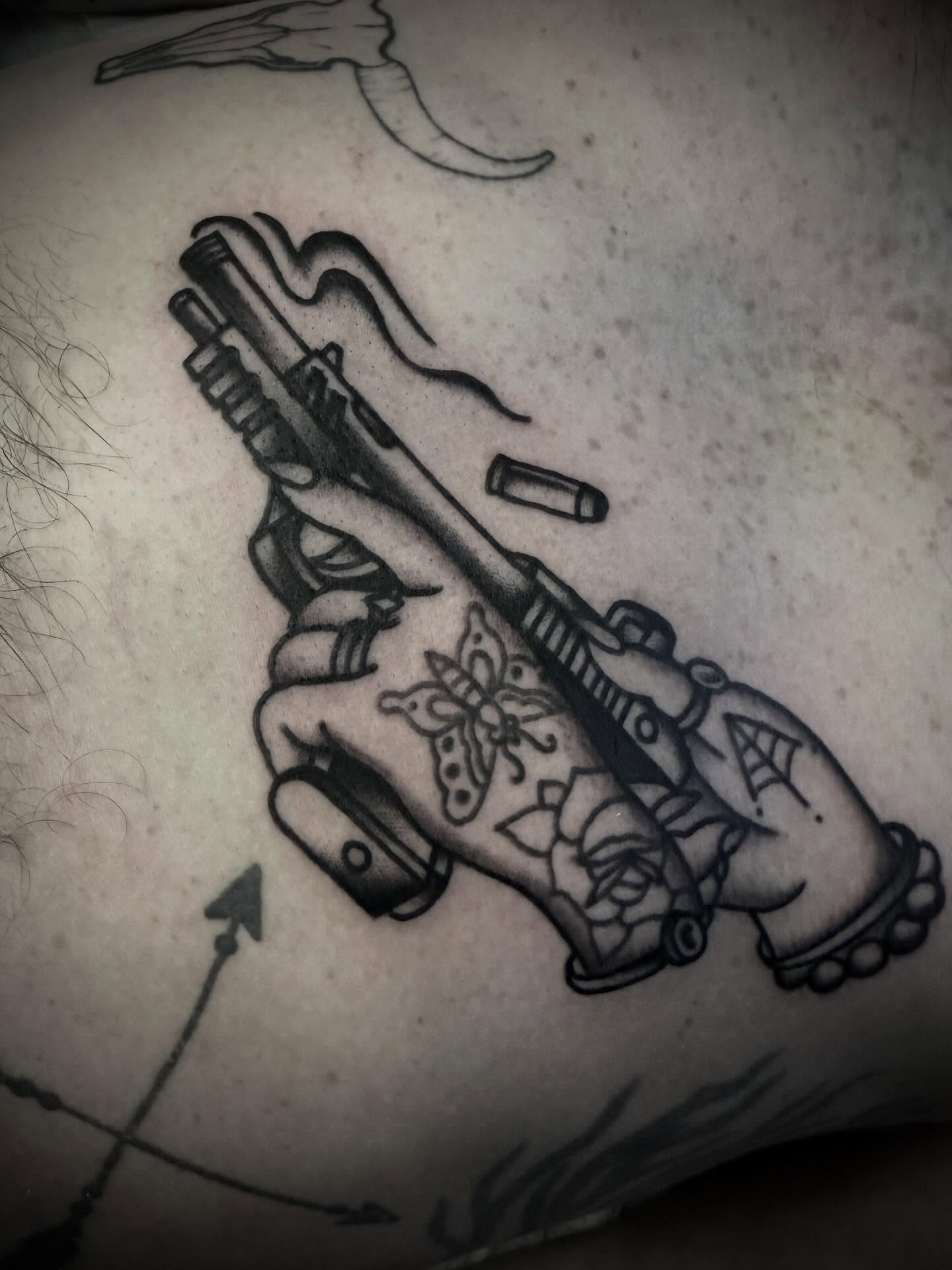 Gun and floral black and grey tattoo on the thigh by Andrew Slater