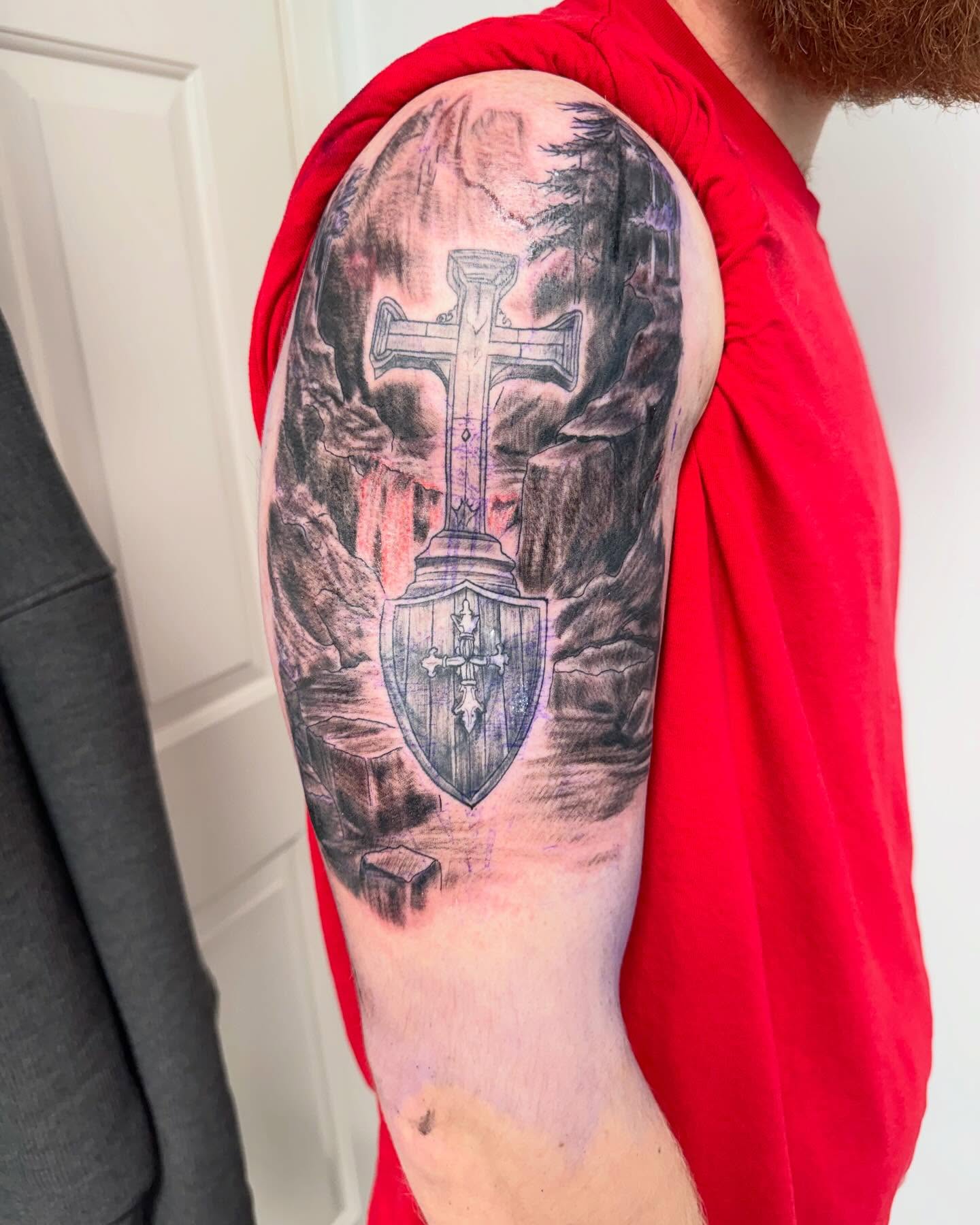 Cross and shield realism tattoo on the upper arm by Brazun Locker Poloschan