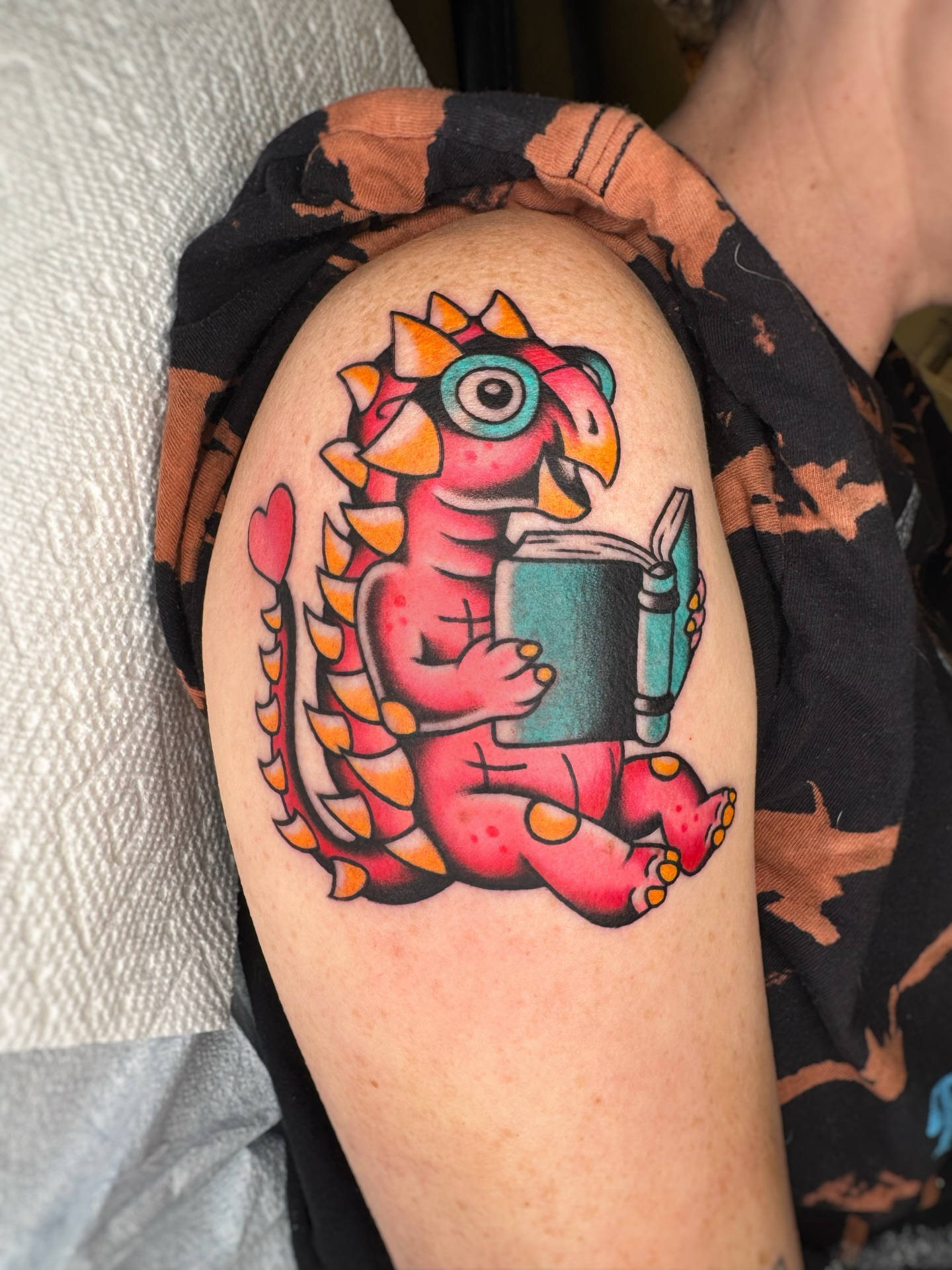 Dinosaur reading book American traditional tattoo on the forearm by Cori James Tattoo Artist