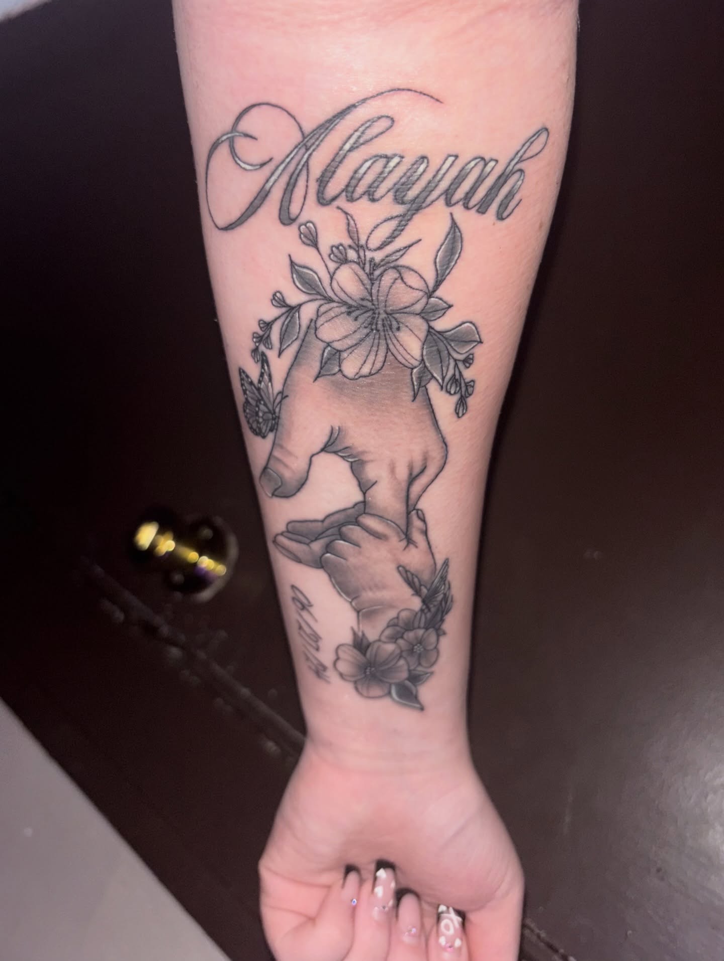 Name with floral design black and grey tattoo on the forearm by Sk Pierce