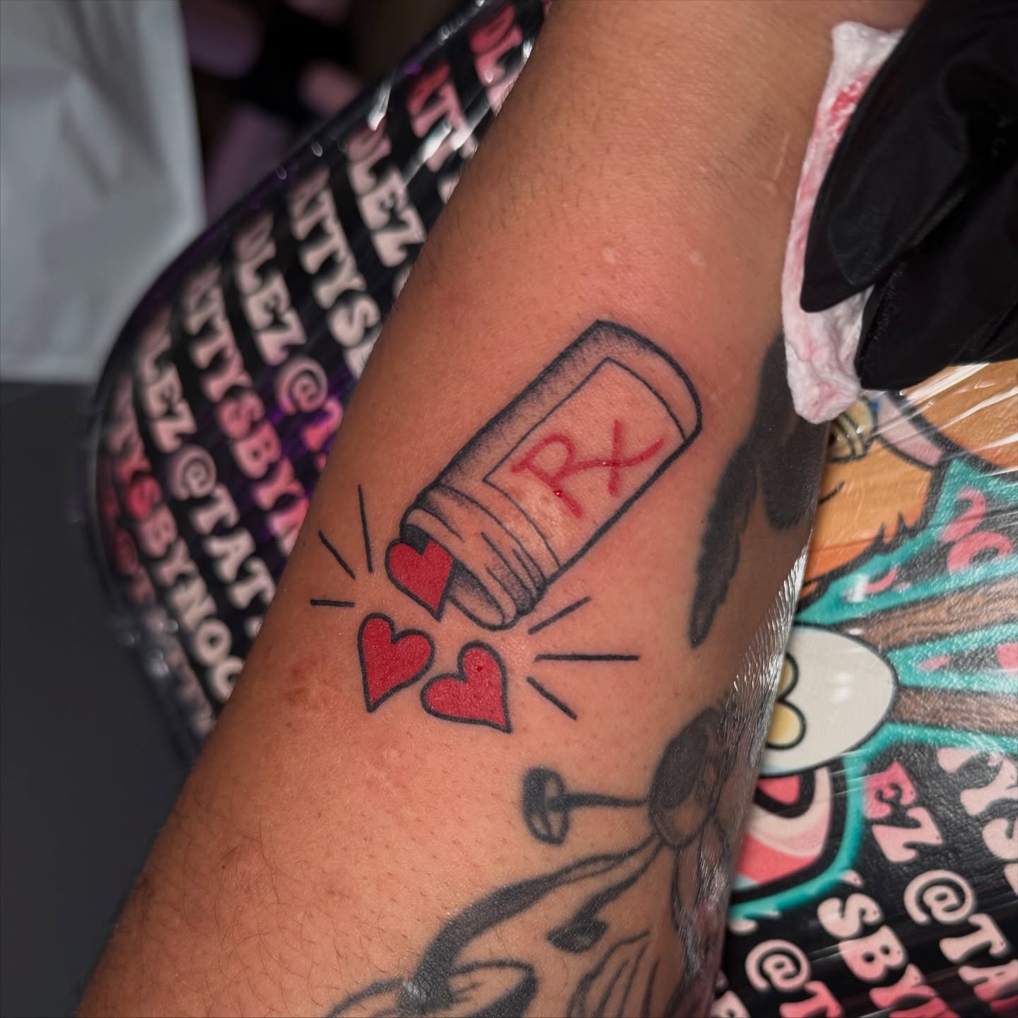 Medicine bottle with hearts new school tattoo on the forearm by Lyndze Masters