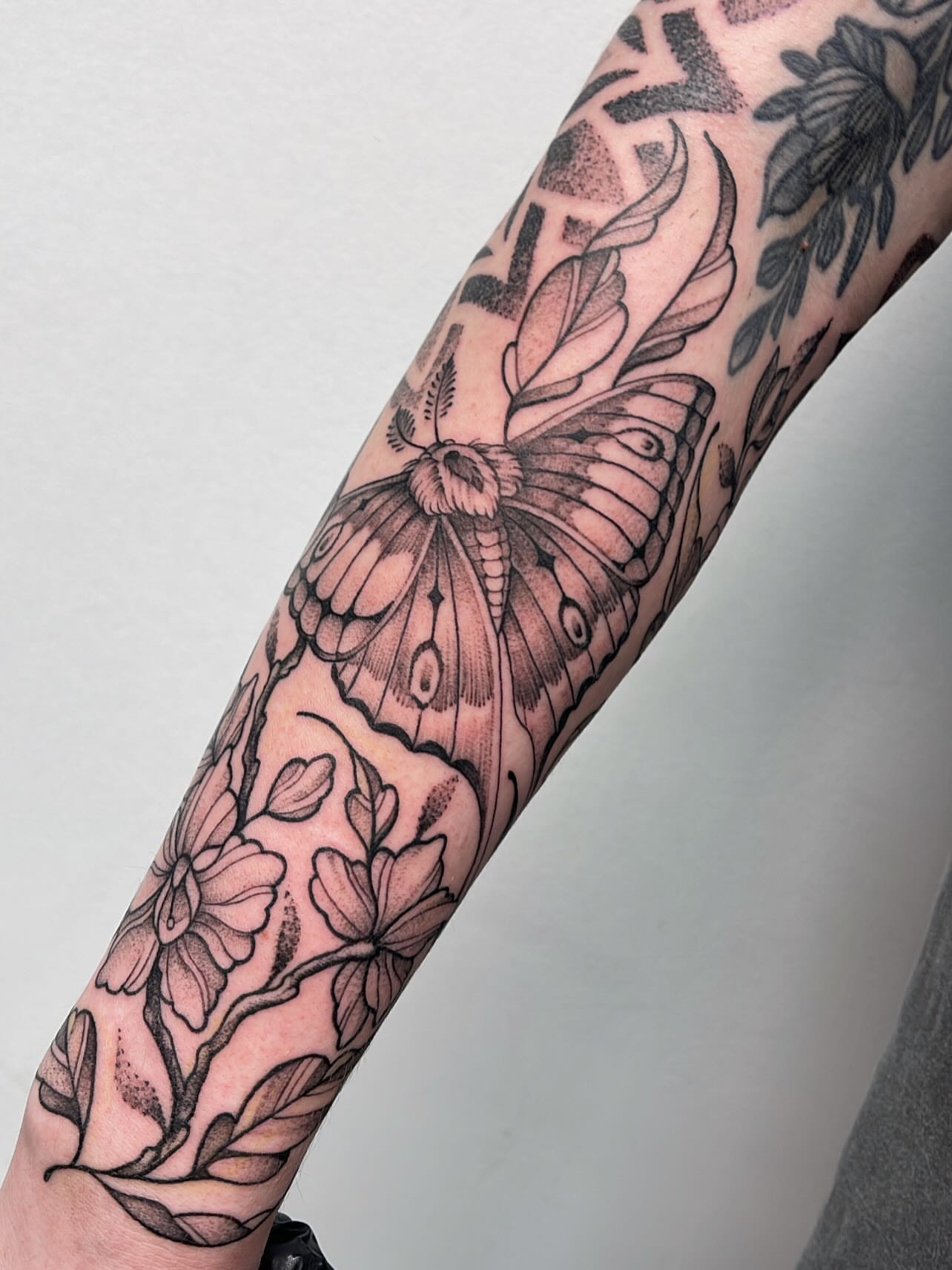 Moth and floral geometric tattoo on the forearm by Miesha Busker