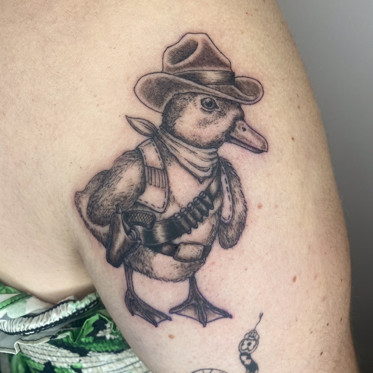 Duck in cowboy attire black and grey tattoo on the upper arm by Melissa Contreras