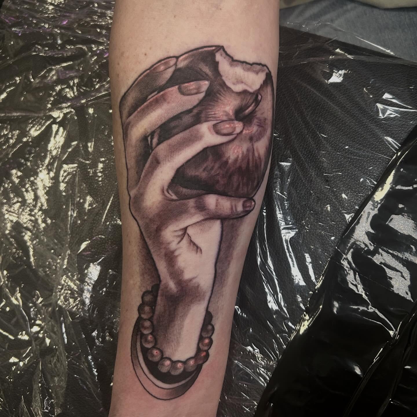 Hand holding heart realism tattoo on the forearm by Whitney Harbin