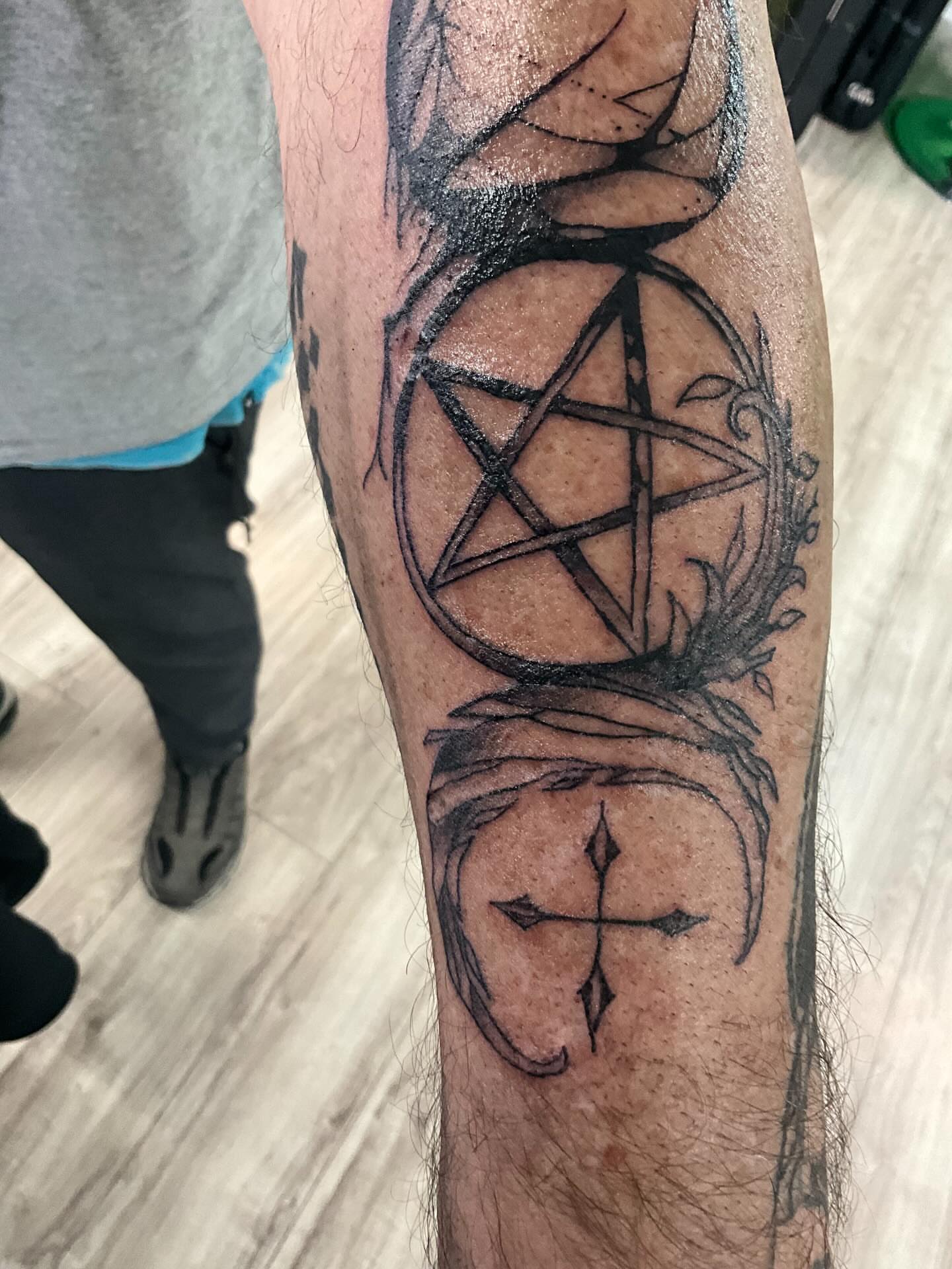 Pentagram and cross black and grey tattoo on the forearm by James Ostler