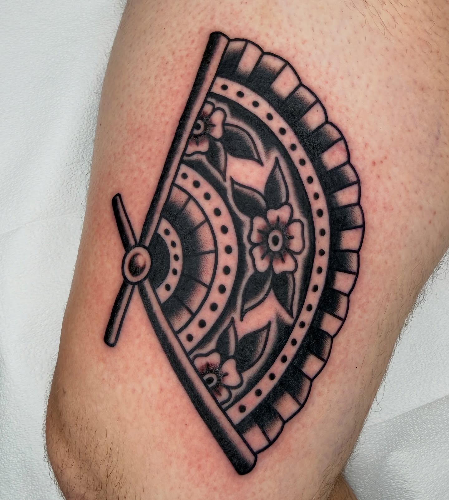 Wheel and floral black and grey tattoo on the forearm by Nick Judkins Tattoo