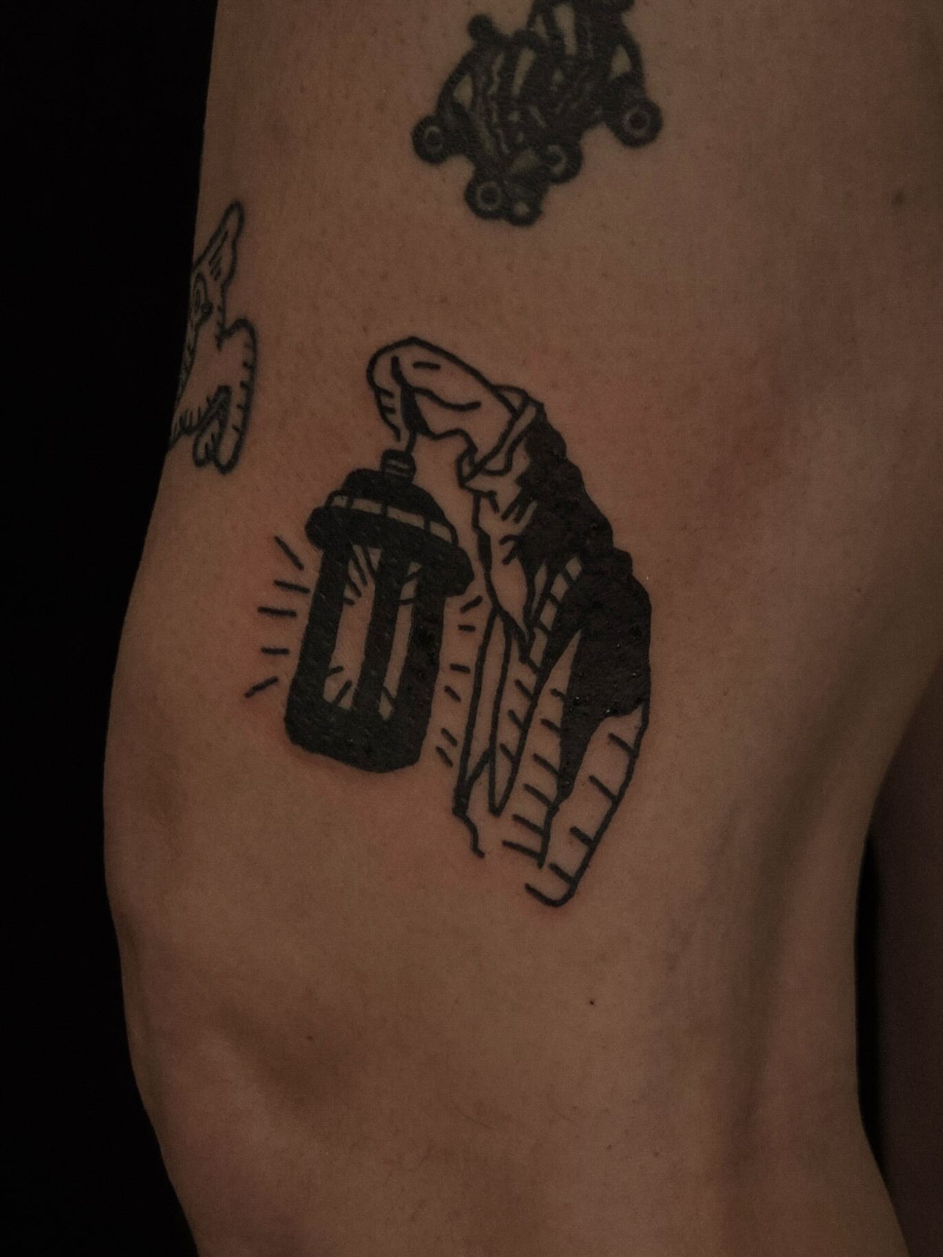 Roller skates and bottle black and grey tattoo on the forearm by ashley blyght