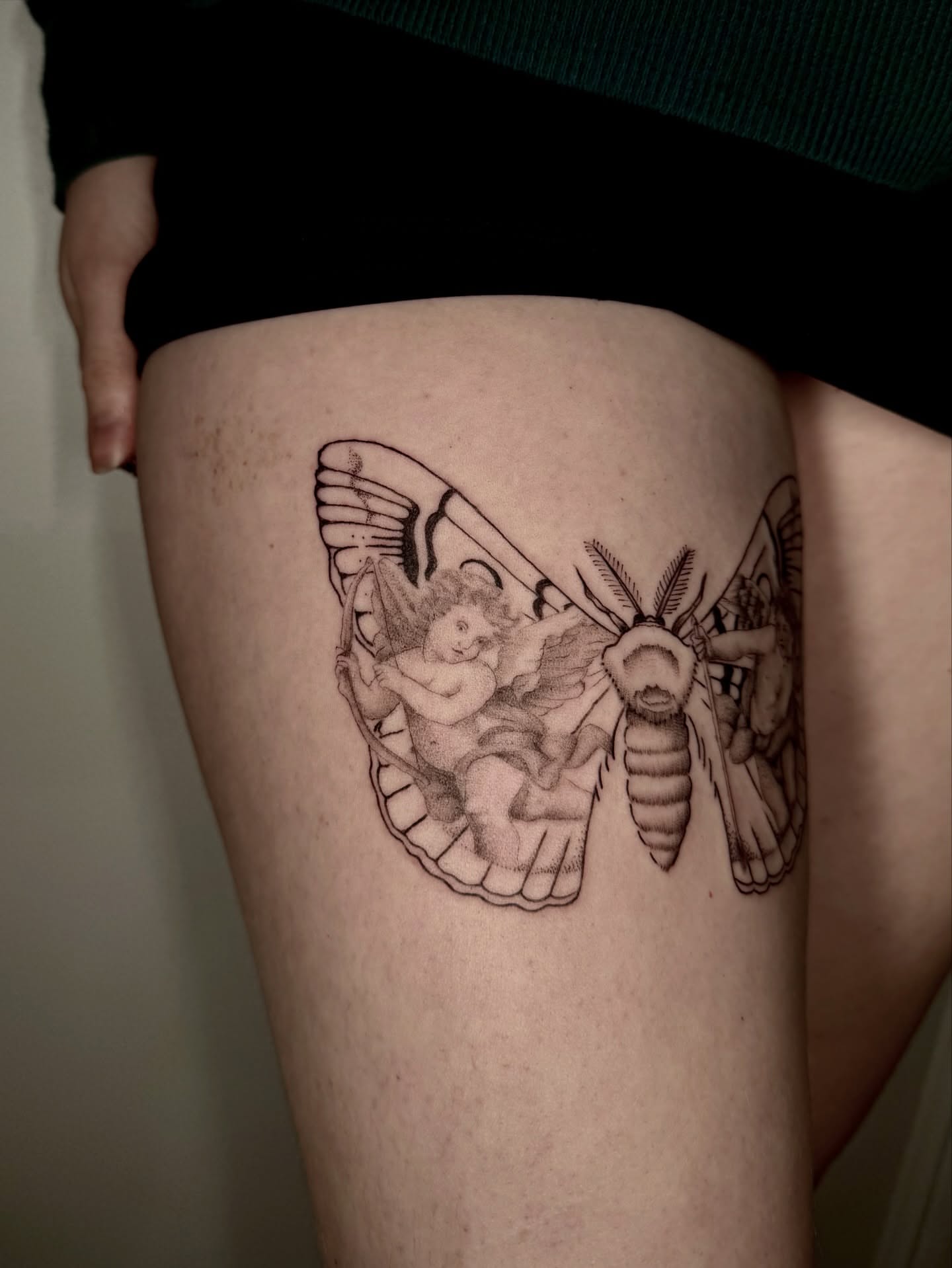 Mythical moth with cherub realism tattoo on the thigh by Ian Saner