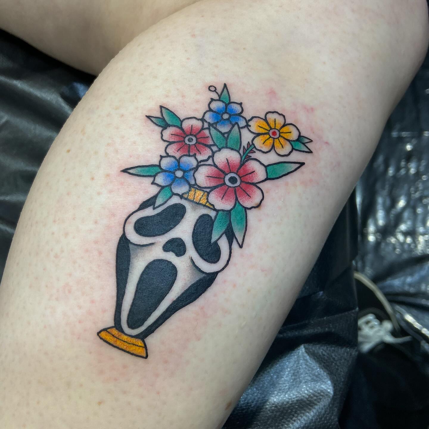 Mask with floral bouquet American traditional tattoo on the thigh by Tattoos by Dale Hupke, Lebanon, Ohio