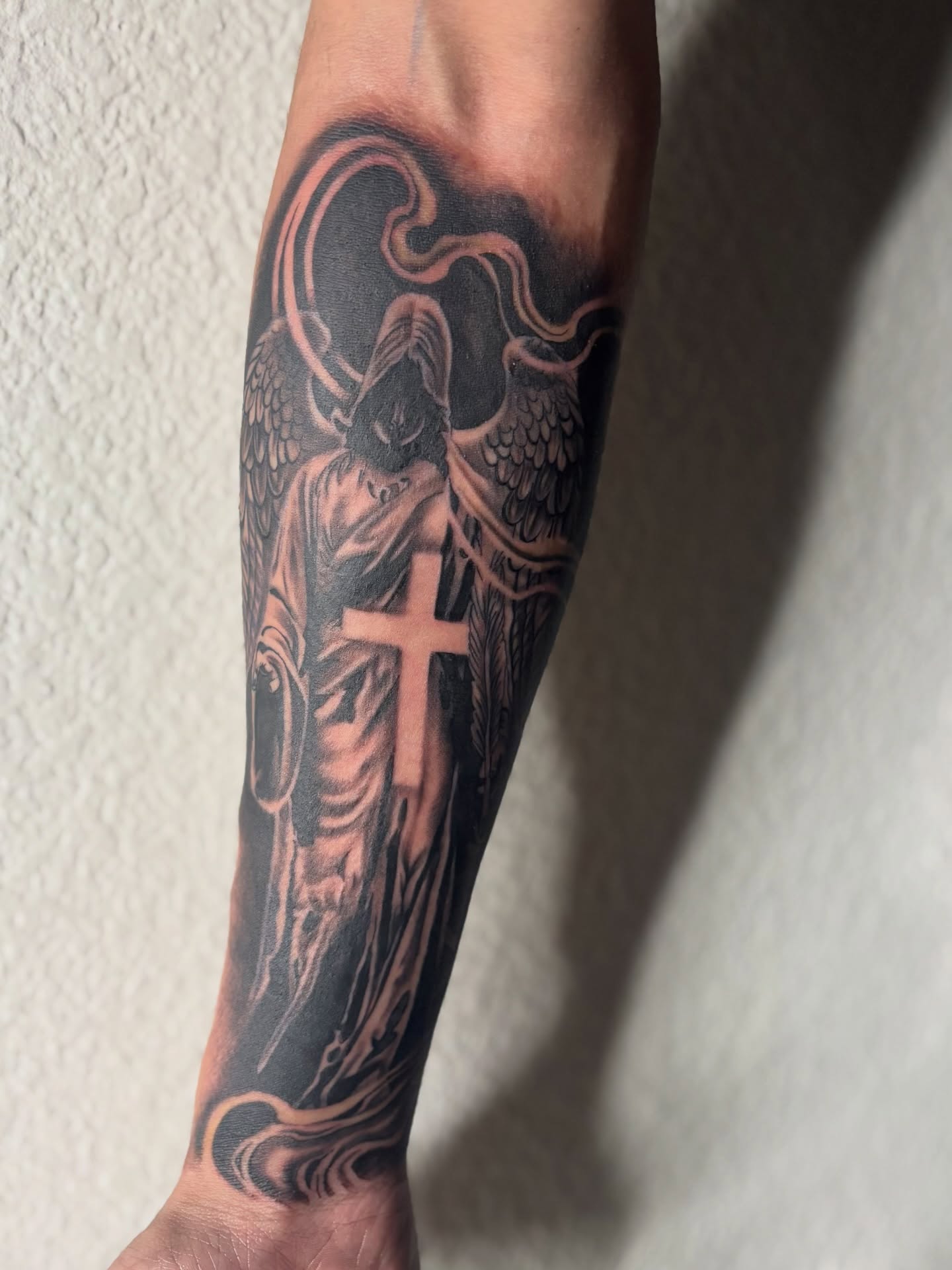 Angel with cross black and grey tattoo on the forearm by @tattoosbyadrian