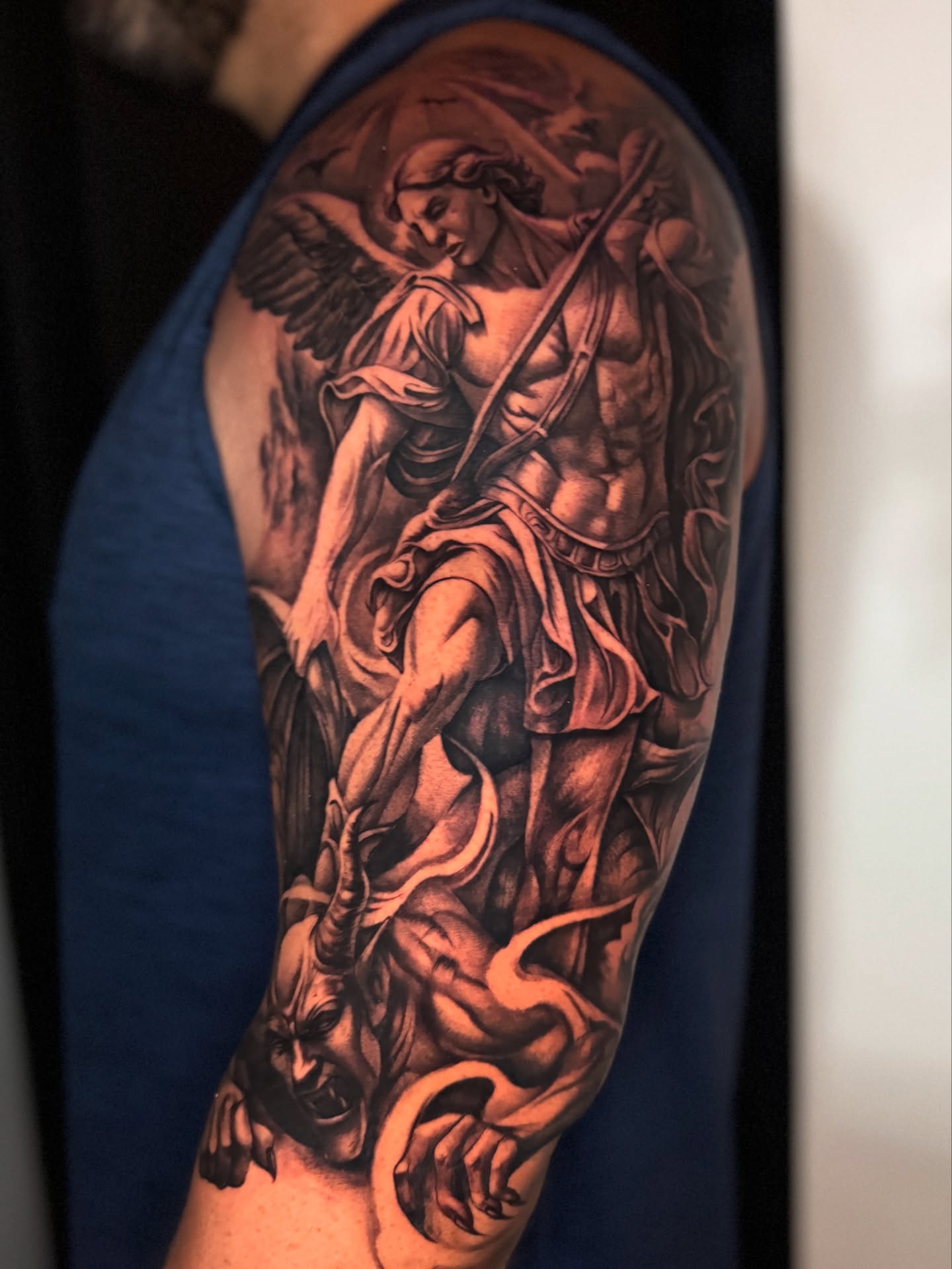 Angel slaying demon realism tattoo on the upper arm by tombstone