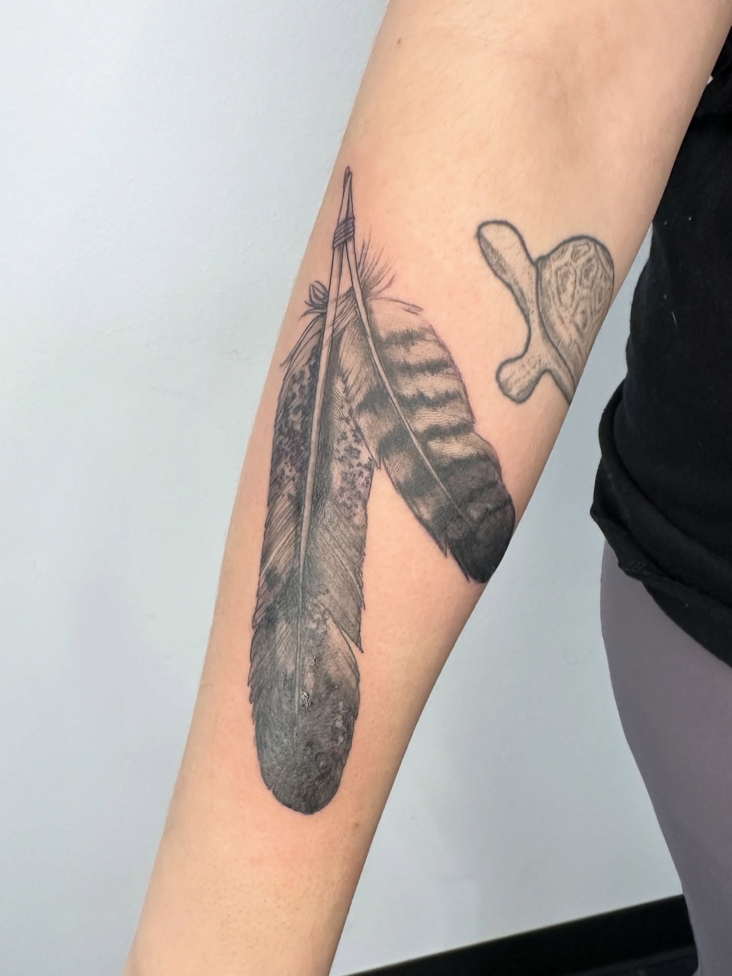 Feather and bone black and grey tattoo on the forearm by ๐ฌ๐๐๐ฏ๐ ๐ฆ ๐๐ฉ๐ฆ๐ท๐๐๐ข๐ฑ๐ฅ ๐ซง๐ผ, Joplin, Missouri