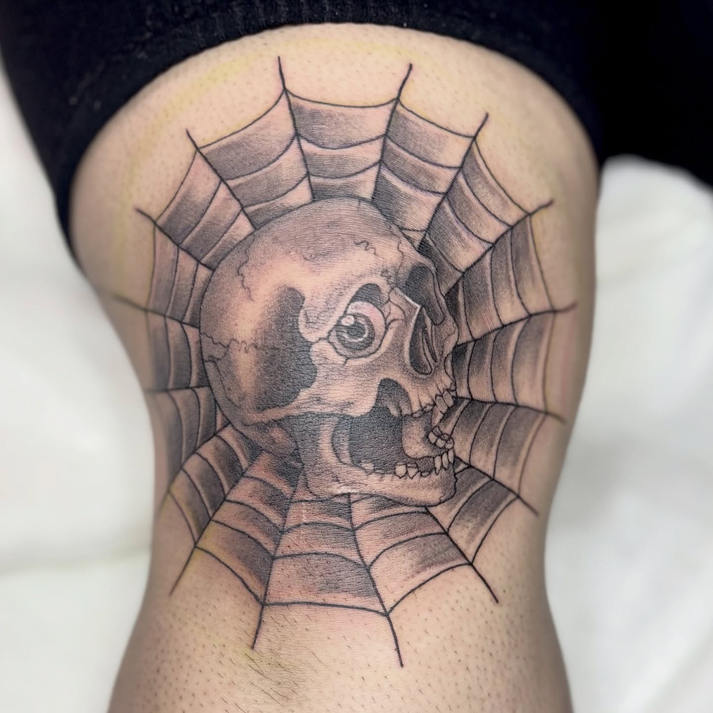 Skull in spiderweb realism tattoo on the thigh by Weho Tattoo Artist Lupe