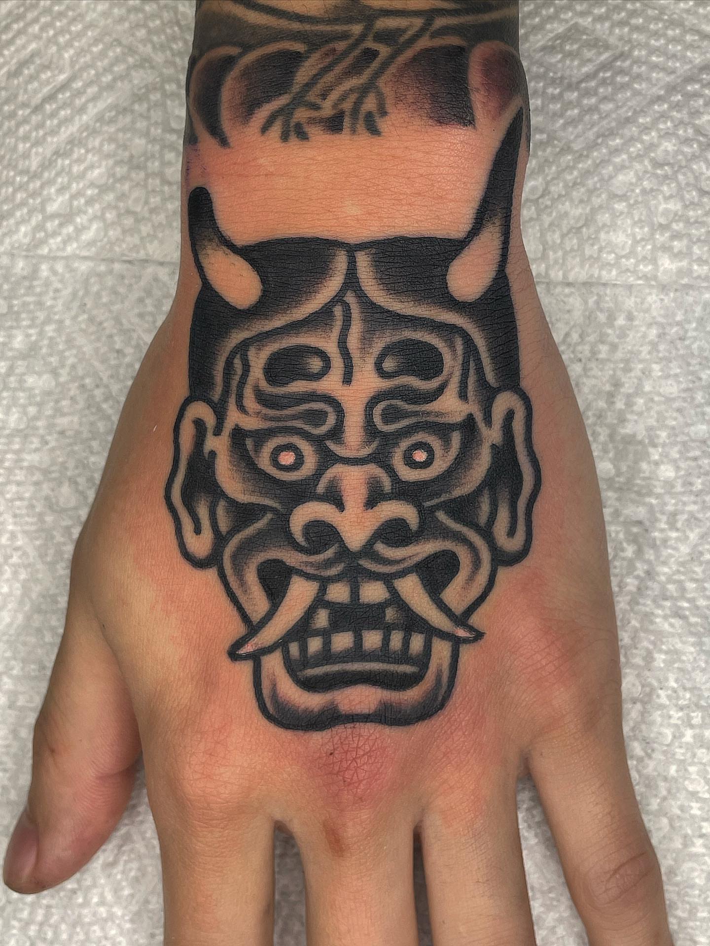 Demon mask black and grey tattoo on the hand by Nicholas M. Passeri