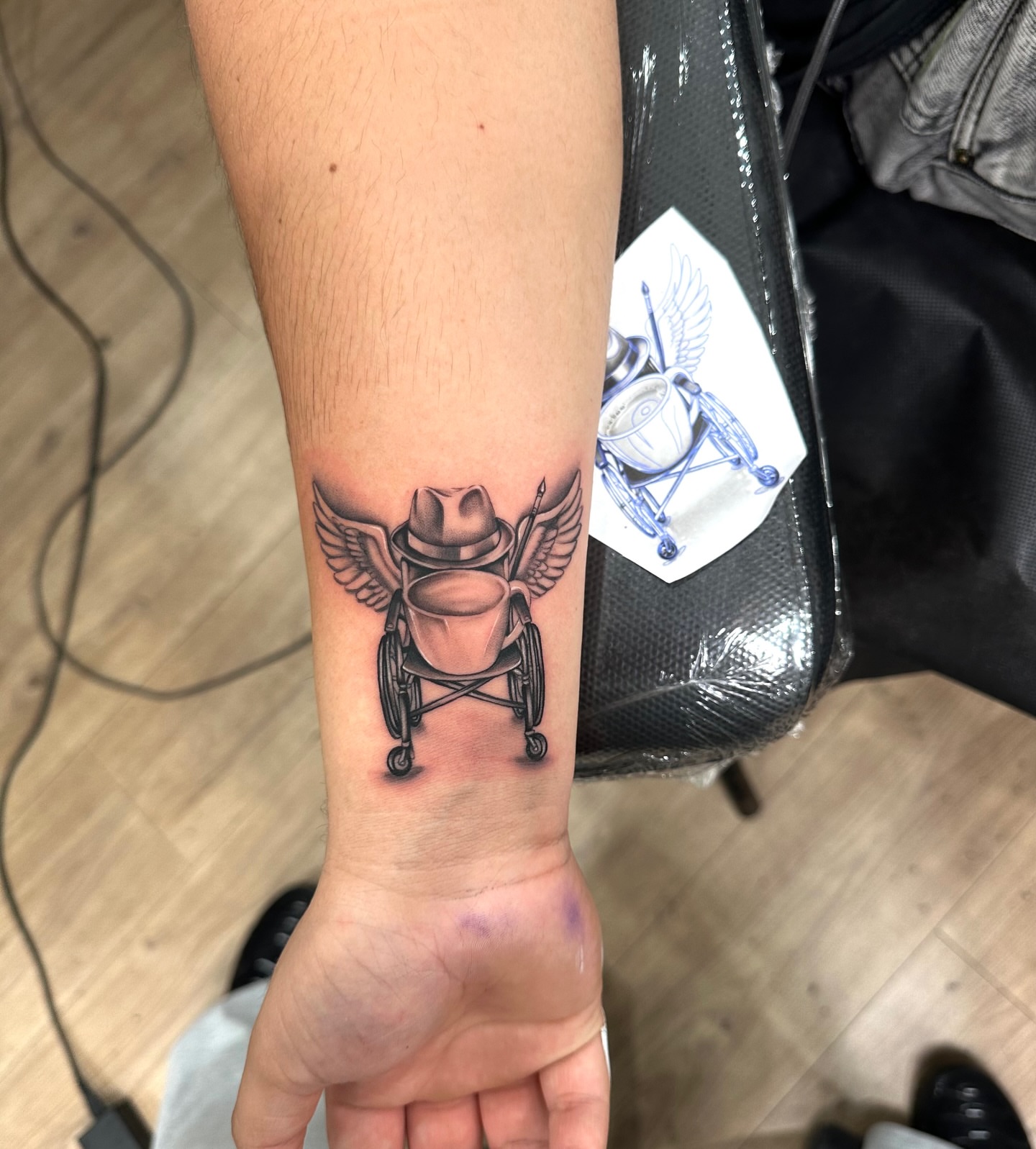 Wheelchair with wings realism tattoo on the forearm by Emma Sferdian🇷🇴