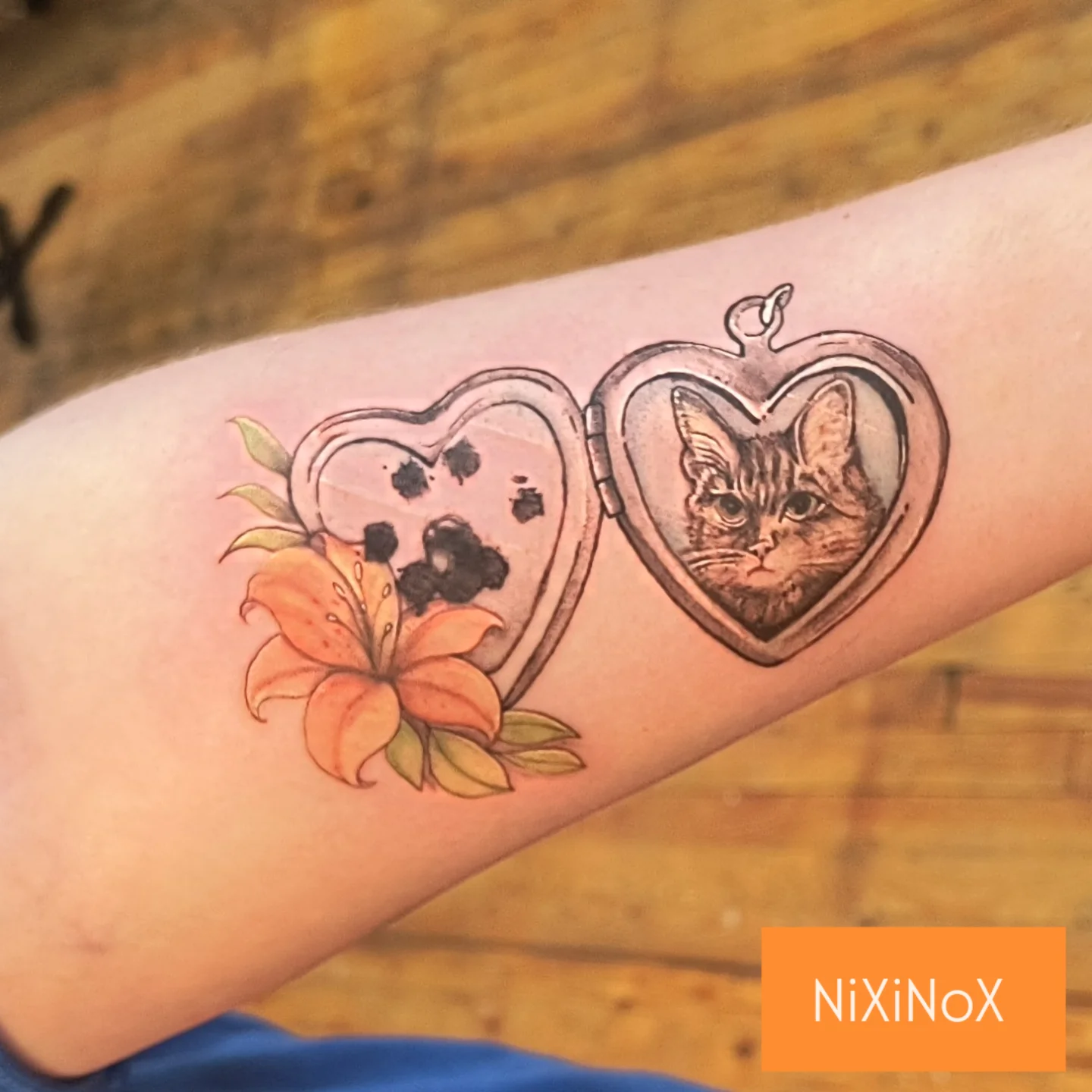 Heart locket with cat and flower realism tattoo on the forearm by Niki Jackson