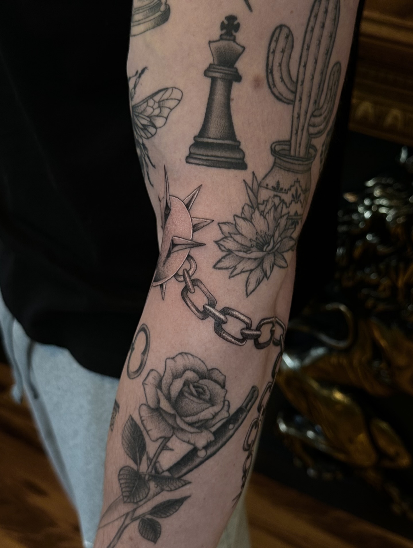 Chess piece, cactus, flower, chain, rose black and grey tattoo on the forearm by Leo Fernandes, Danvers, Massachusetts