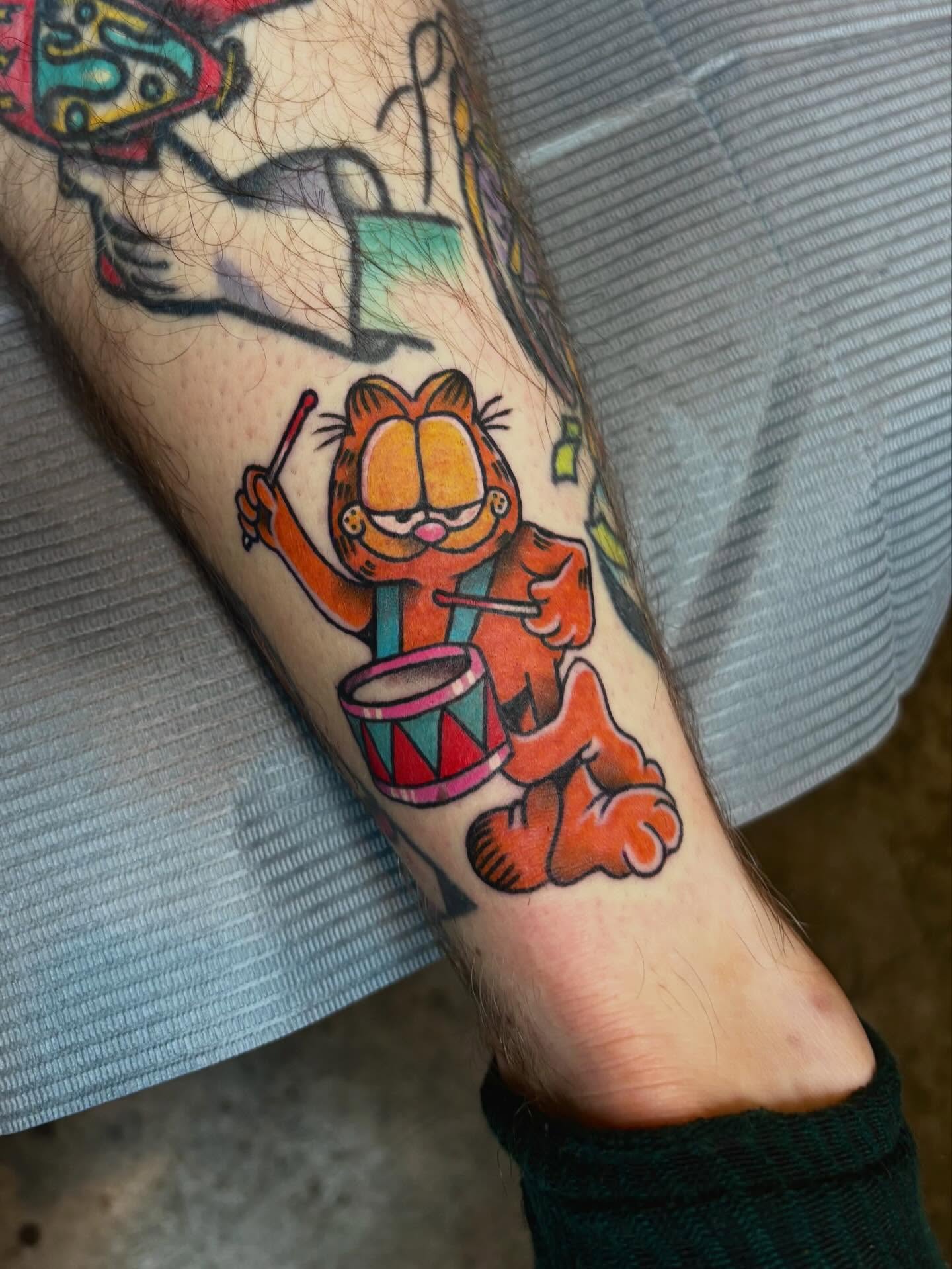 Garfield playing drums American traditional tattoo on the forearm by Mim