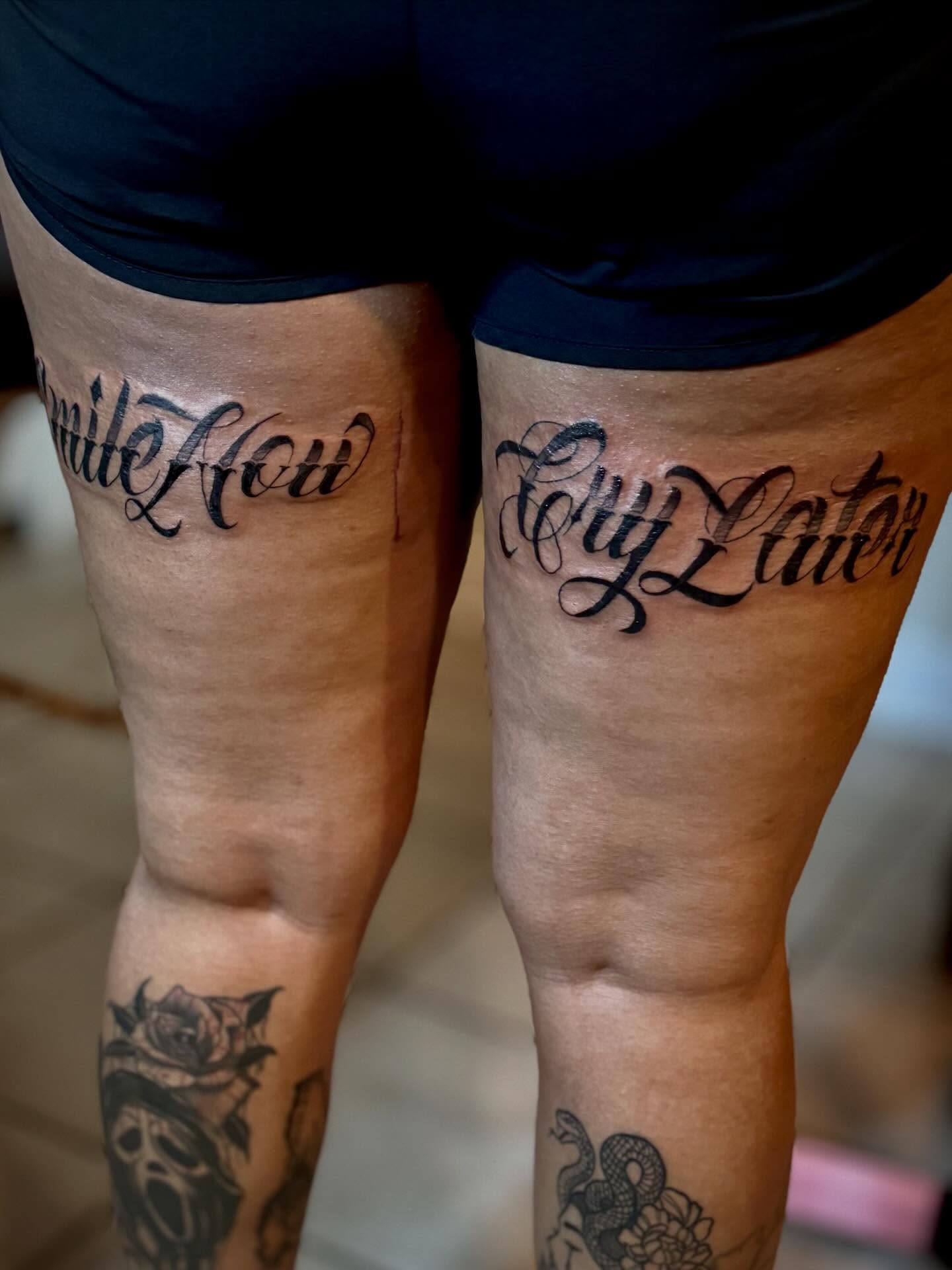 Smile now cry later lettering script tattoo on the thigh by Katelyn Arnold