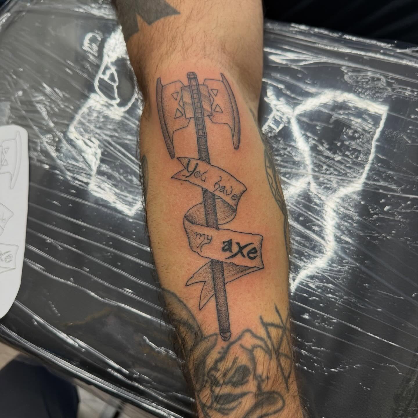 Ax with banners black and grey tattoo on the forearm by Matt Hattaway