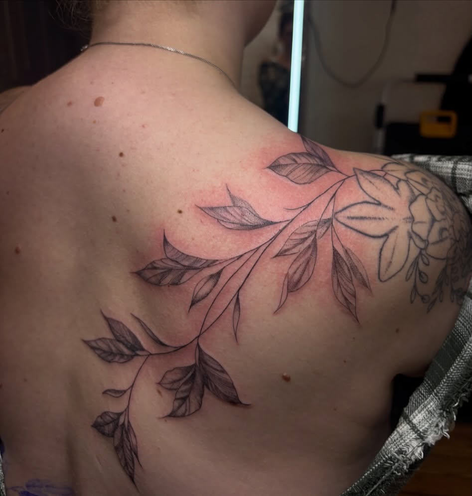 Branch with leaves black and grey tattoo on the shoulder by Sydney Gallucci