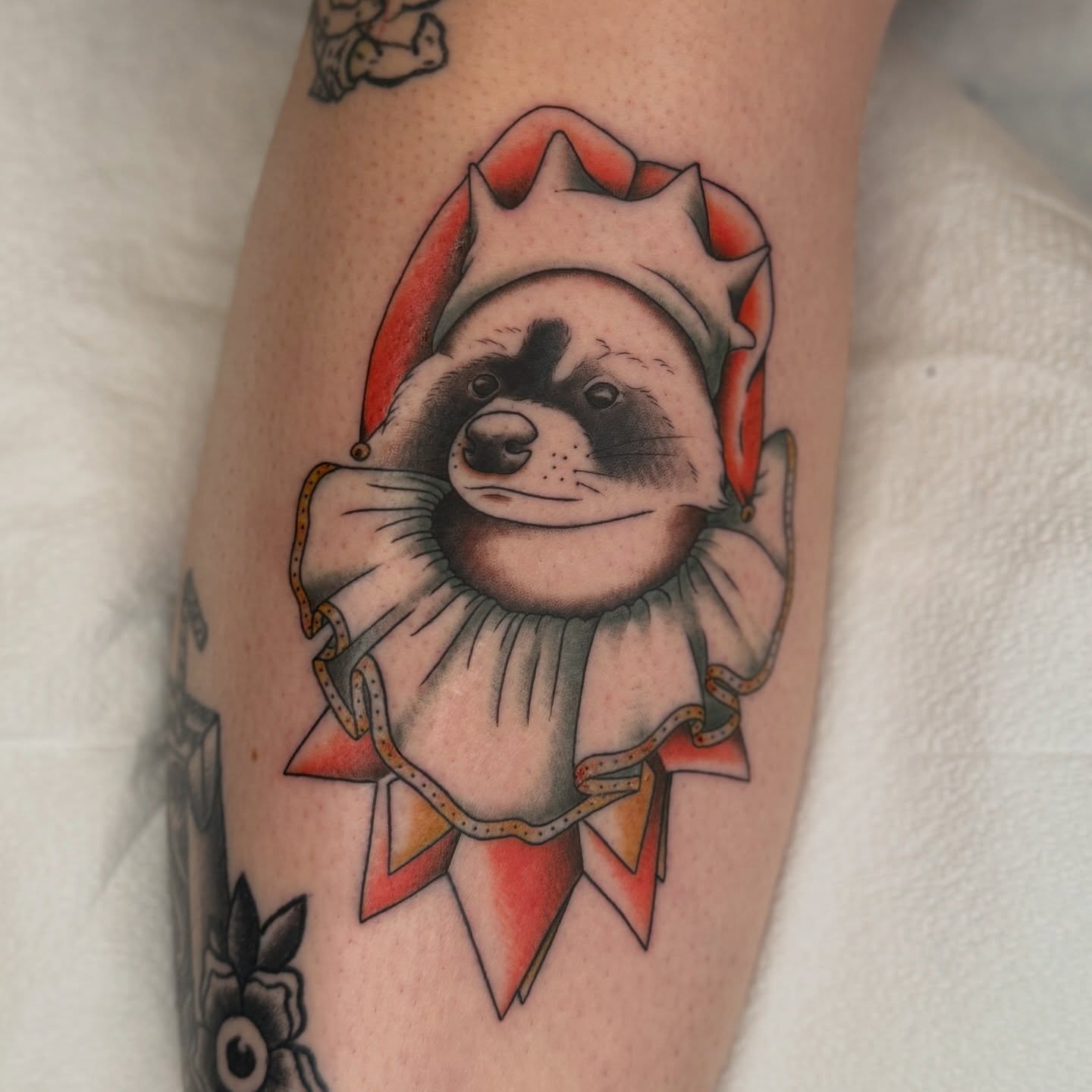 Raccoon clown American traditional tattoo on the forearm by Maddie Hammell